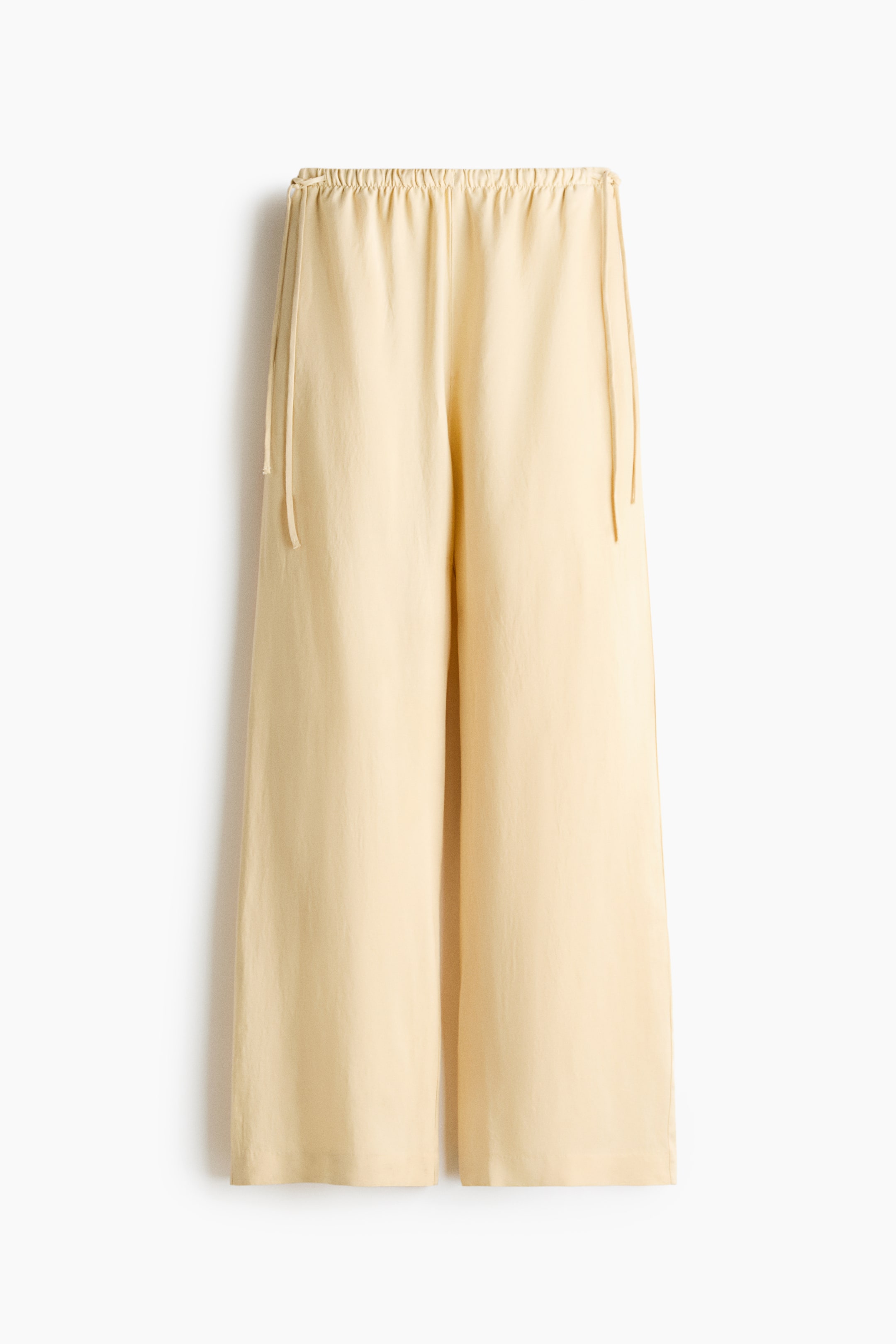 View larger image: Light-coloured, loose-fit trousers are shown from the front. They feature a high, elasticized waist with a double-ended drawstring and wide legs.