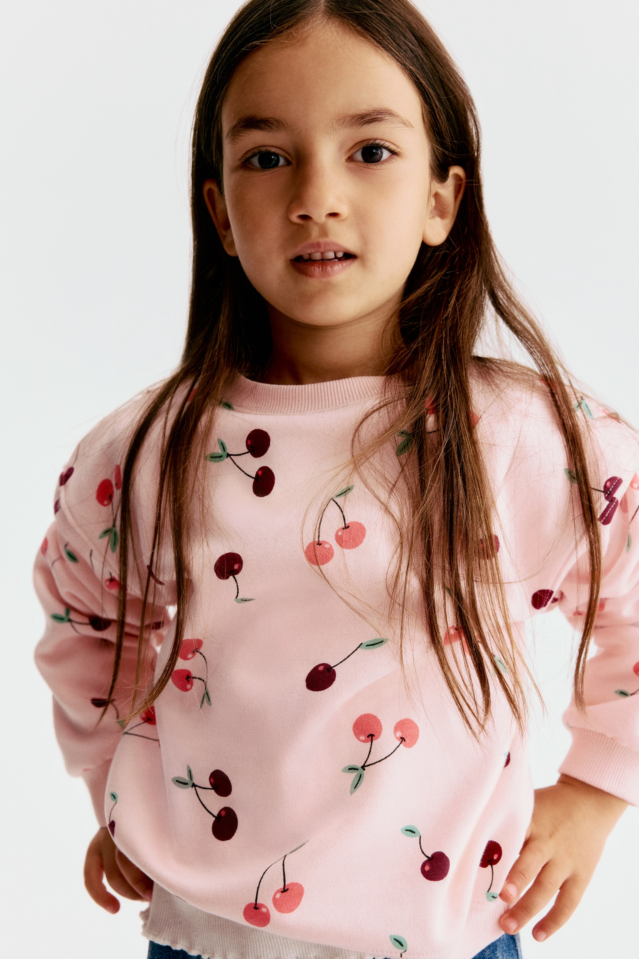 View larger image: A light pink sweatshirt with an all-over cherry print is shown from the front, highlighting its ribbed crew neckline, dropped shoulders, and ribbed cuffs.