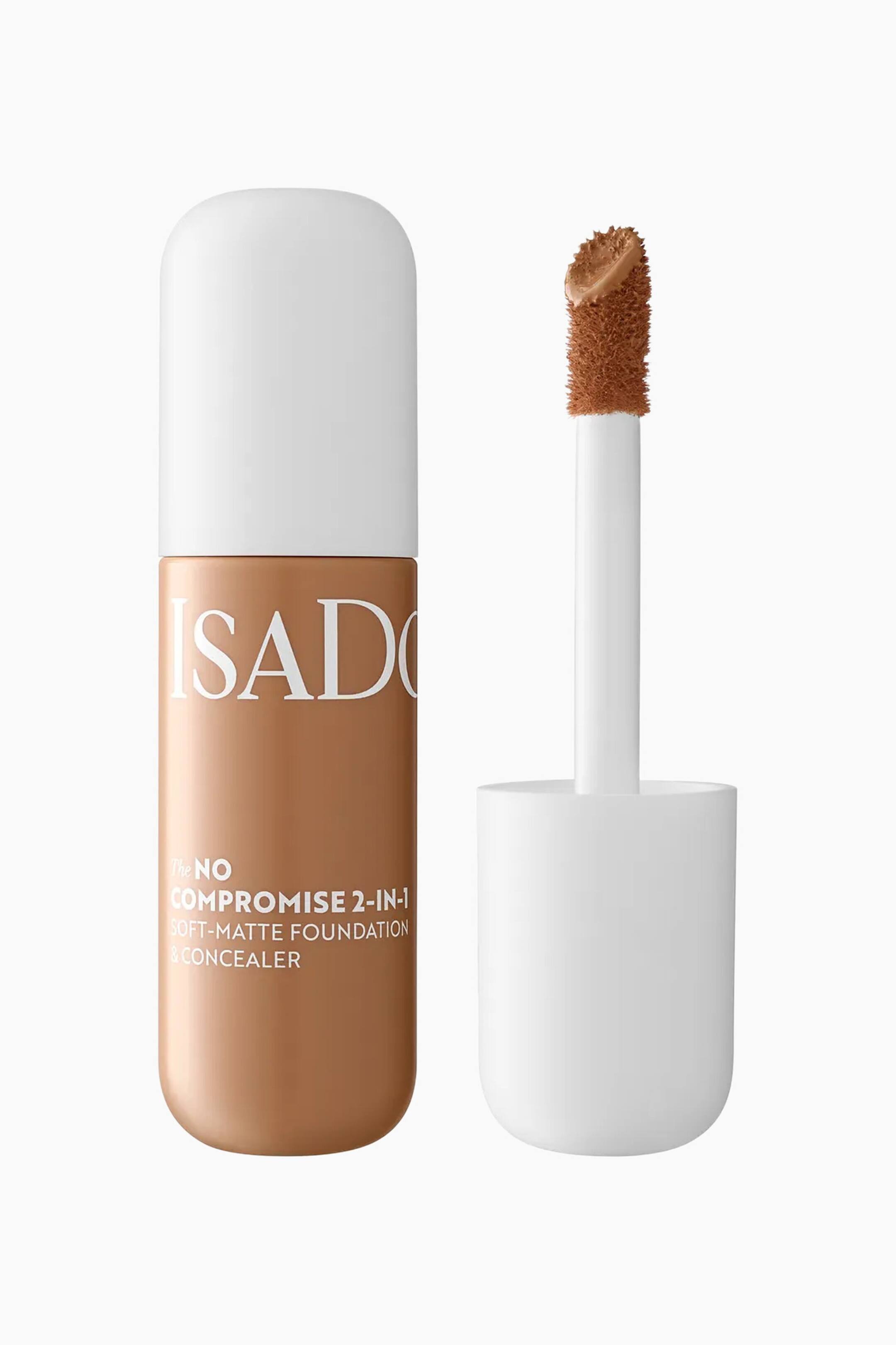 Se større billede: En flaske IsaDora 2-in-1 foundation og concealer står lodret ved siden af sin afskruede applikatorstav. Den cylindriske flaske har en afrundet hvid hætte og indeholder en medium-tan flydende formel, mens den separate hvide stav viser en stor, vinklet doe-foot applikatorspids, der er dækket af den samme tan-farve.