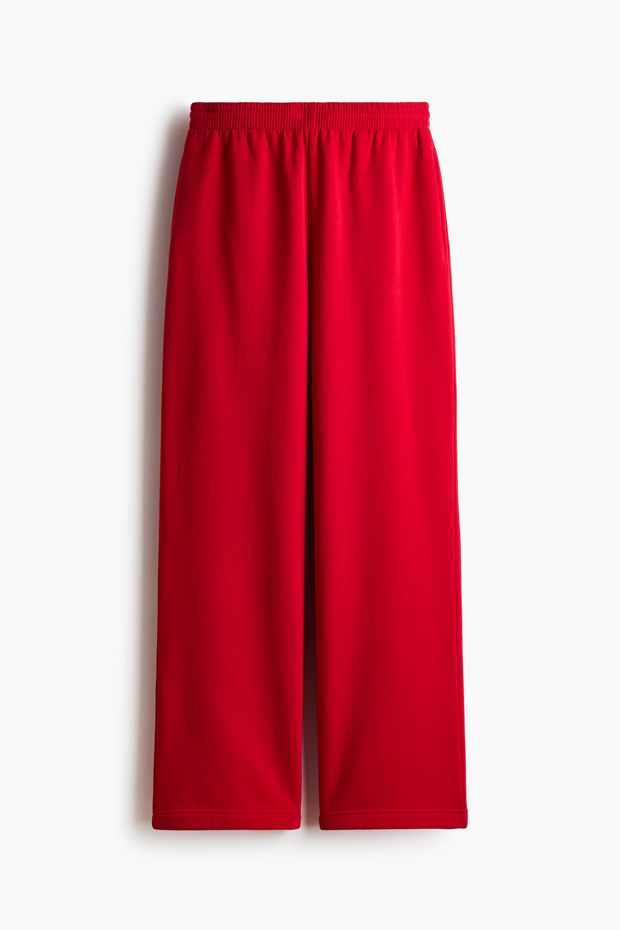 View larger image: Red track pants are shown in a front view, featuring a smocked elastic waistband, subtle side pockets, and loose, straight-cut legs.