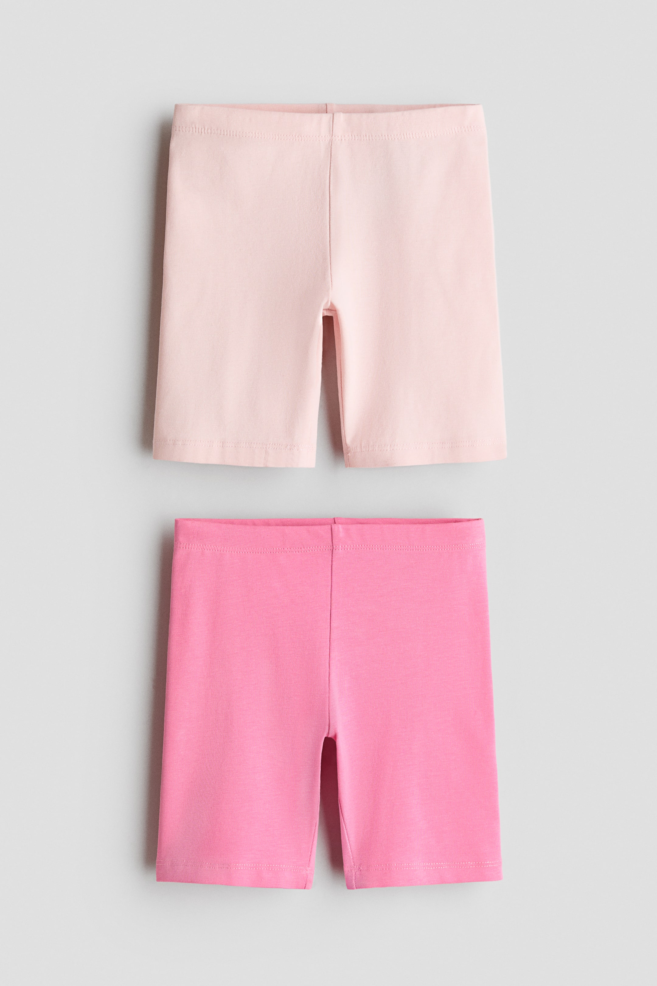 View larger image: Two pairs of jersey shorts are displayed facing forward, featuring elastic waistbands and hemmed leg openings, with one pair in light pink and the other in bright pink.