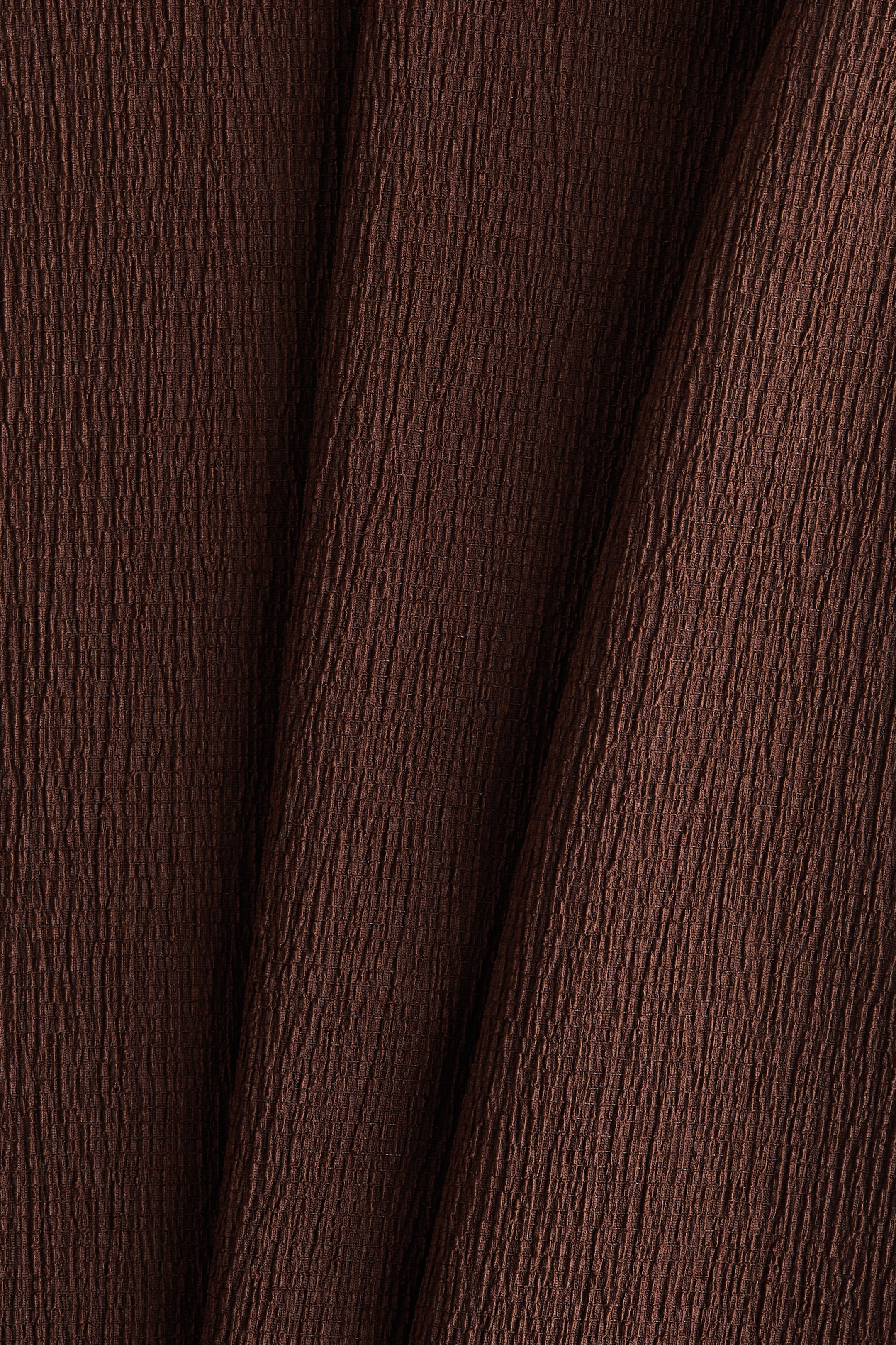 View larger image: A dark brown fabric is displaying a finely crinkled texture, with soft folds creating variations in light and shadow across its surface.