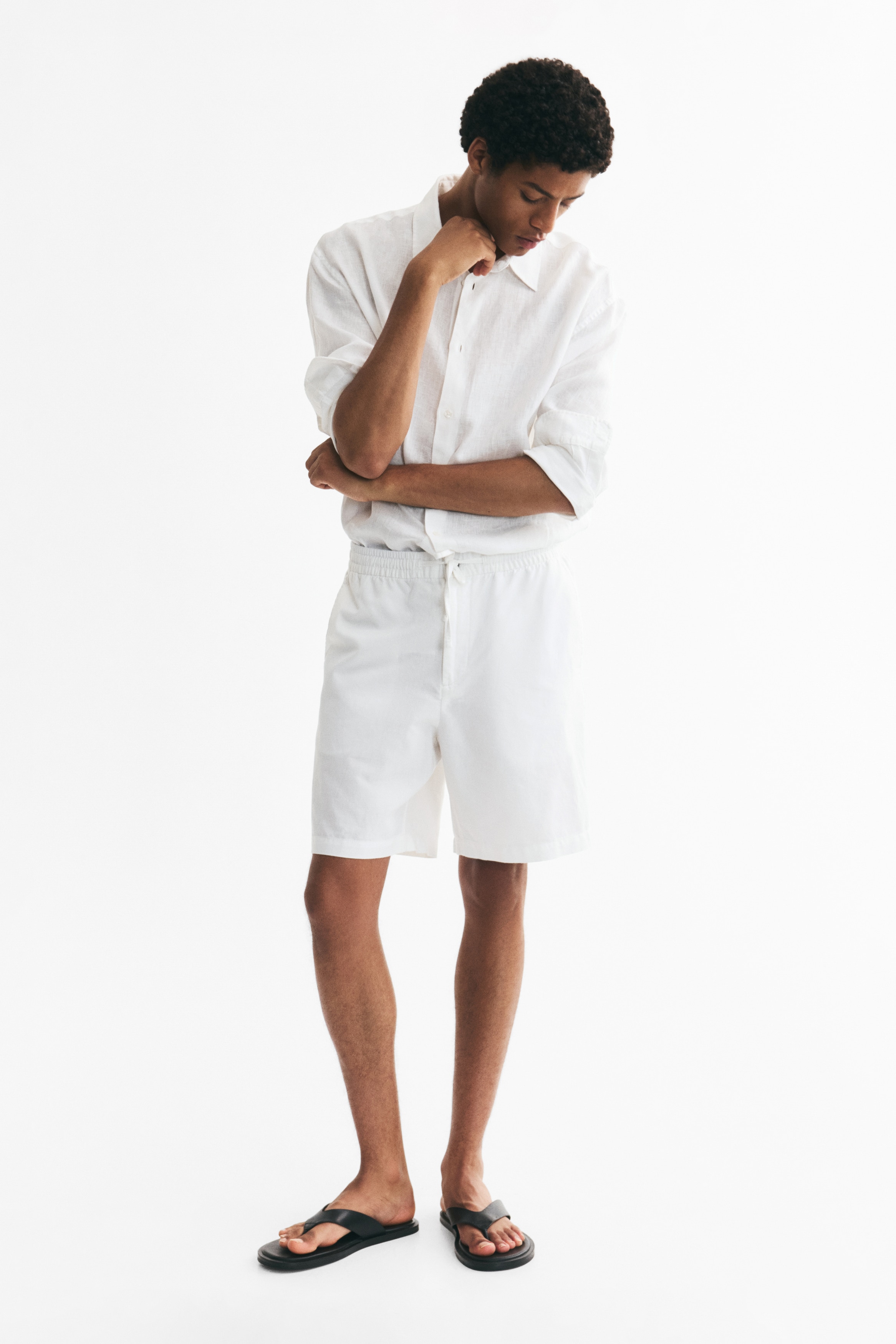 White shorts crafted from a textured cotton and linen blend are showcased from the front, featuring an elasticated waist with a drawstring and button closure, along with side seam pockets.