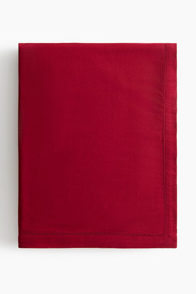 A red cotton tablecloth is lying folded flat, displaying its smooth weave, a decorative hemstitching border, and a wide finished hem. - 1