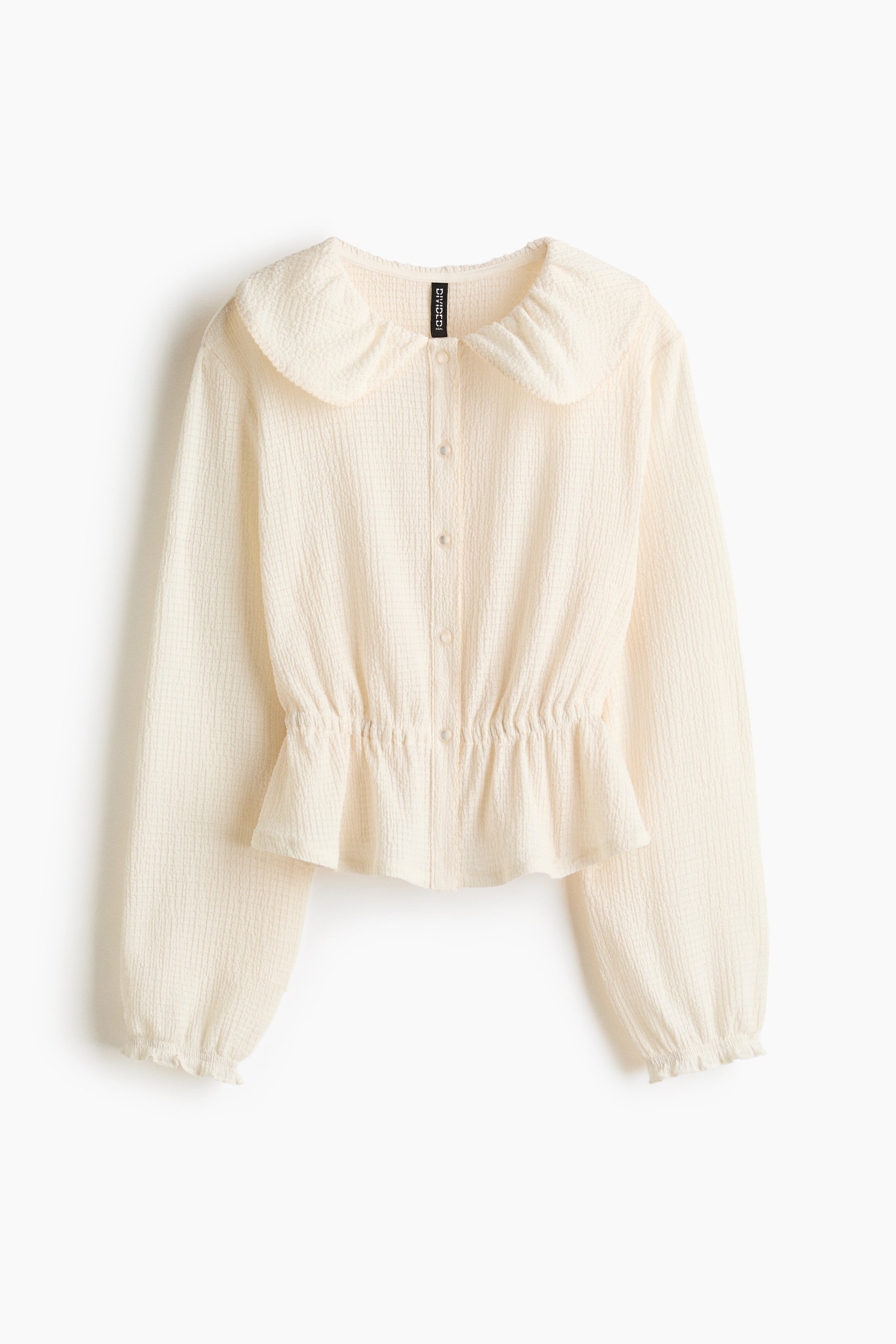 View larger image: A cream-textured jersey top features a picot-trimmed Peter Pan collar and a button band down the front. It is cut with gently dropped shoulders, long sleeves with elasticated, overlocked edges at the cuffs, and covered, gathered elastication at the waist, creating a flared peplum.