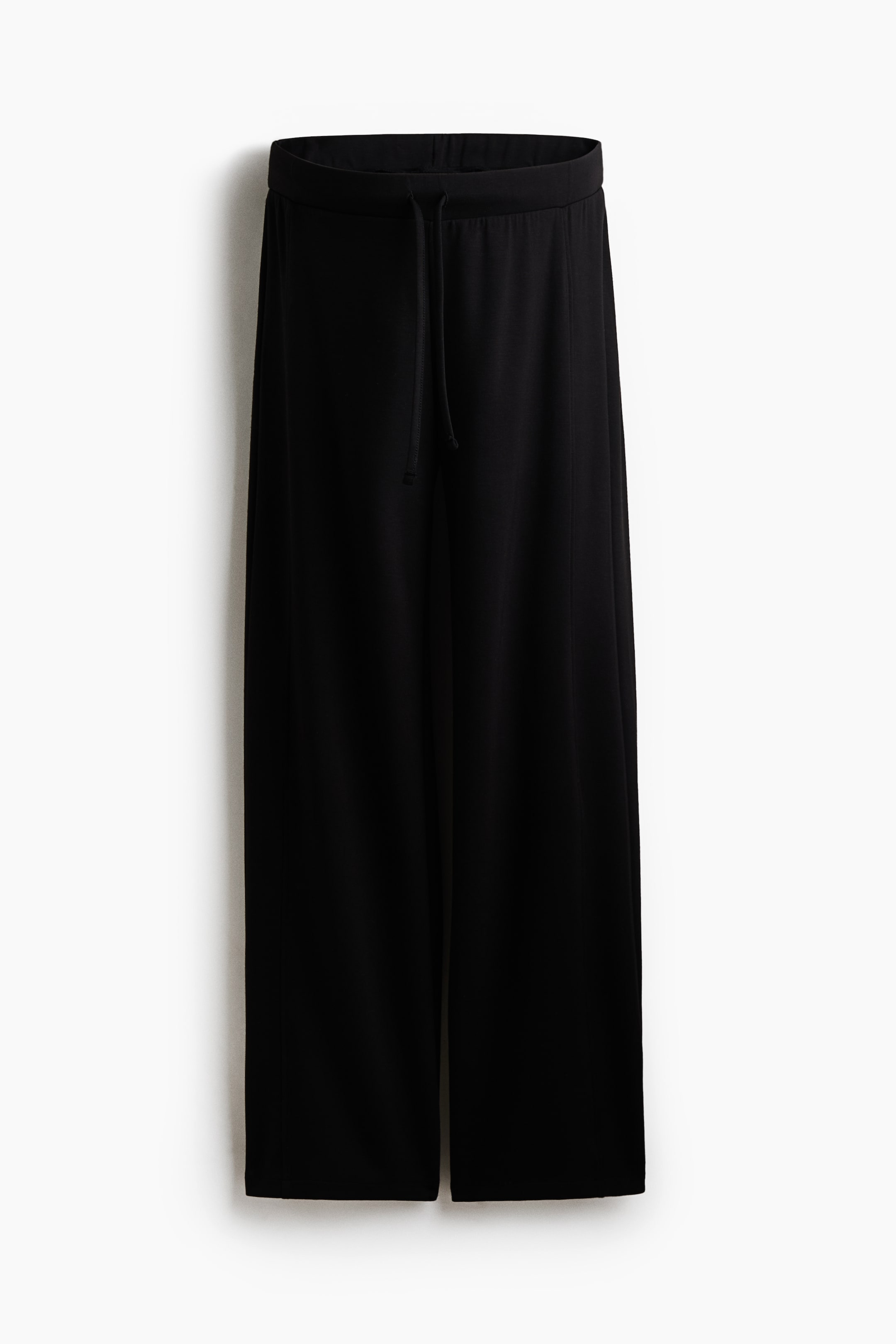 Größeres Bild anzeigen: Ein Paar schwarze Wide-Leg-Hosen hängt frontal und zeigt einen elastischen Bund mit einem farblich passenden Kordelzug in der Mitte. Der leichte Stoff fällt gerade nach unten und betont ein entspanntes, locker geschnittenes Design.