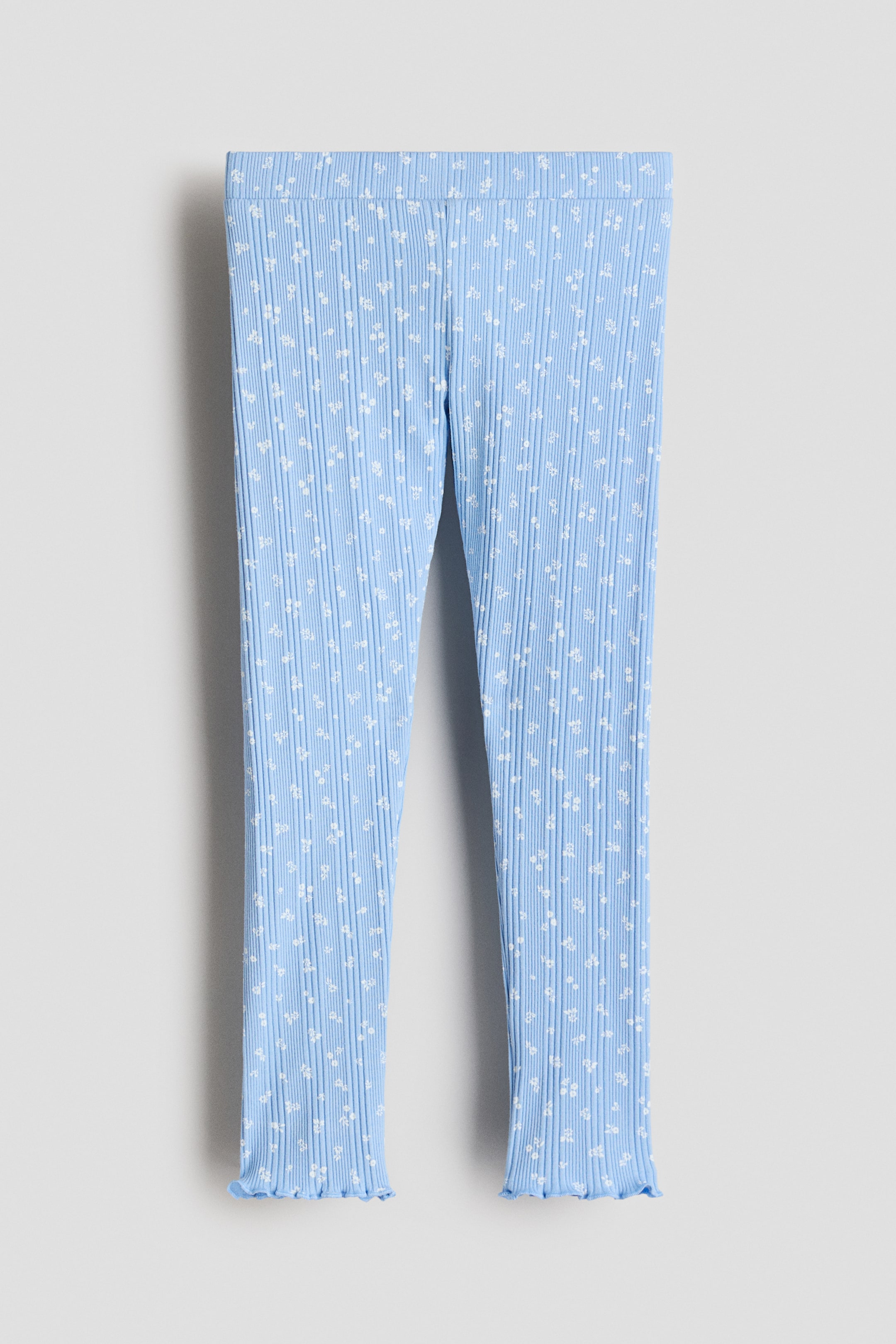 View larger image: Light blue ribbed knit leggings display a delicate white floral pattern, featuring a flat waistband and ruffled lettuce-edge hems at the ankles.