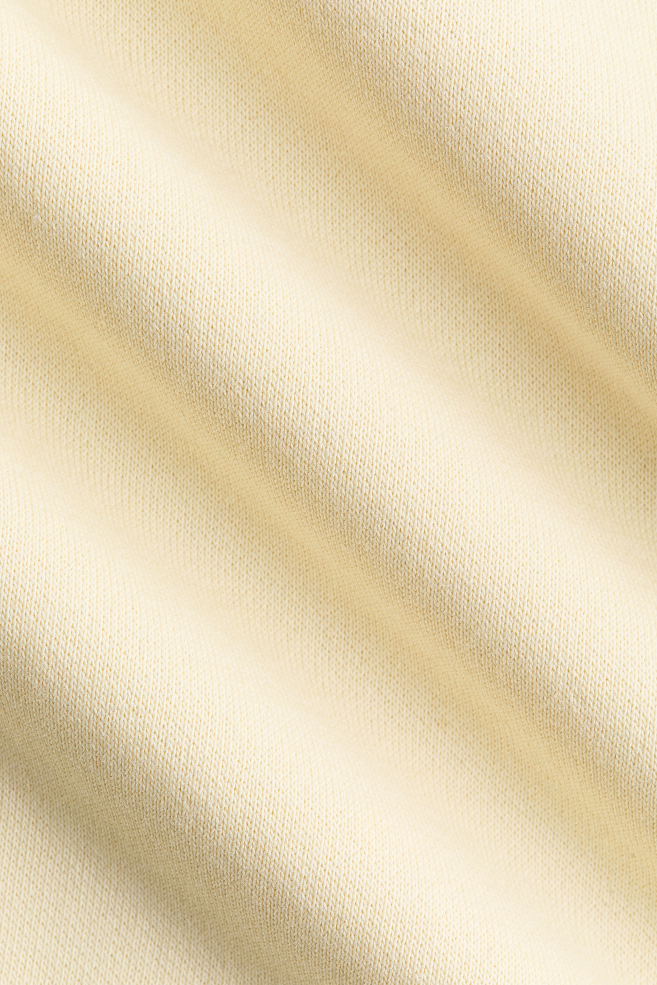Größeres Bild anzeigen: Der hellgelbe Strickstoff zeigt eine feine, gleichmäßige Textur mit weichen, diagonalen Falten.