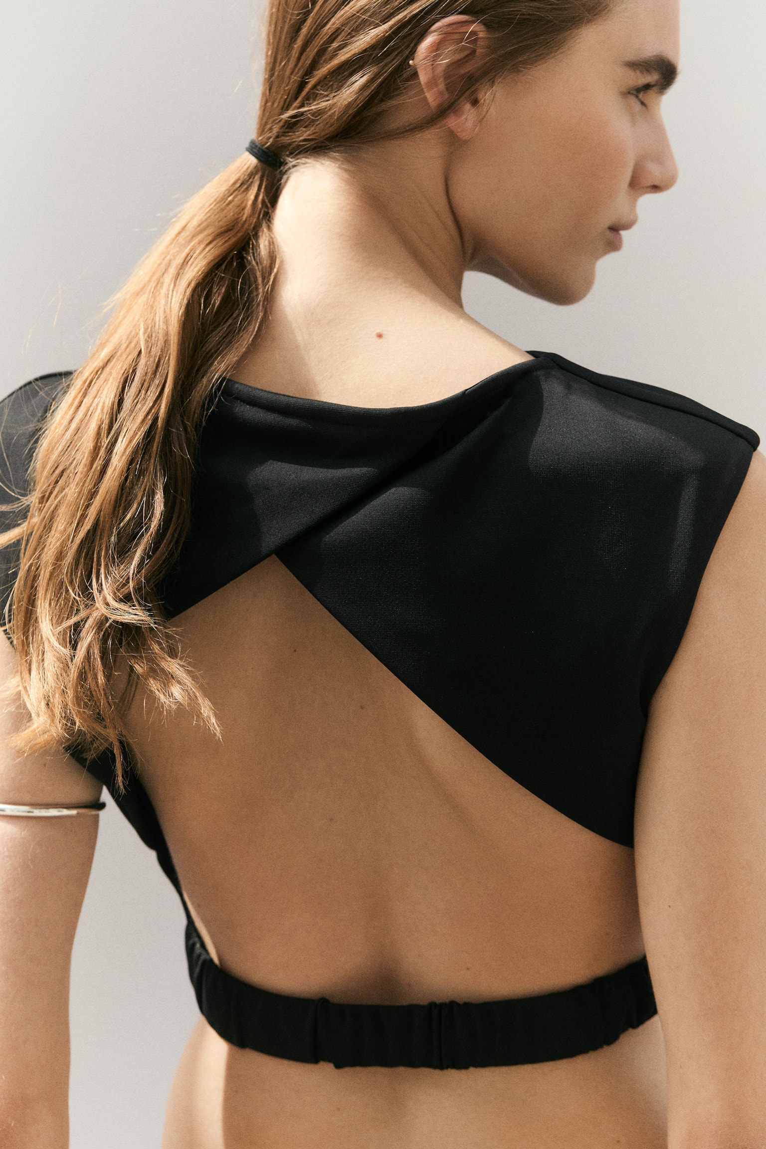 A black top is showcased from the front, featuring a boat neck and short cap sleeves. A straight, cropped hem completes the design, and a white "H&M EDITION" tag is visible at the back of the neck. - 1