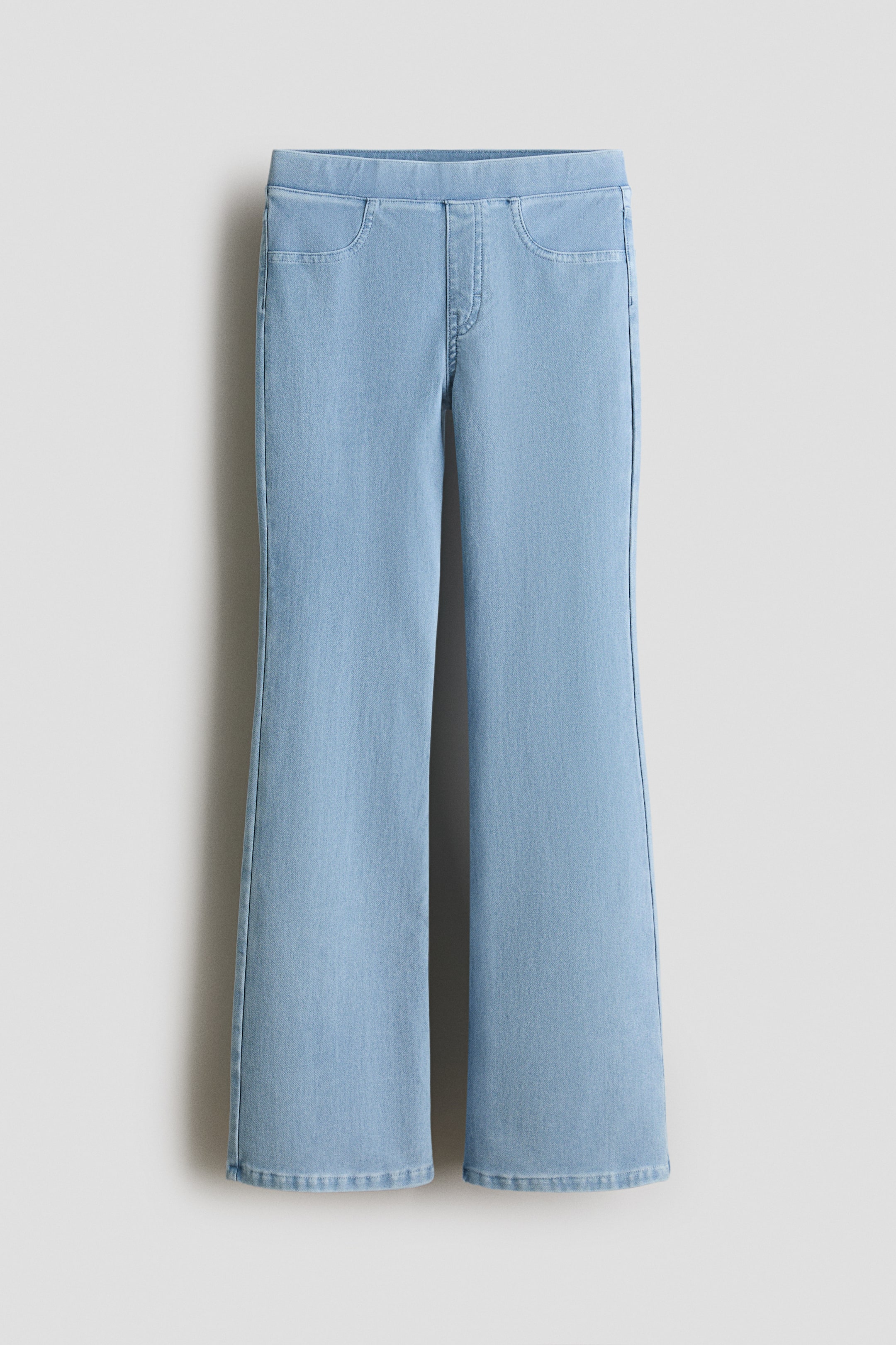 Agrandir l'image: Les jeggings sont présentés DE FACE : ils sont en jersey bleu clair, aspect denim, avec des jambes évasées, une taille élastiquée, une fausse braguette et des poches avant décoratives.