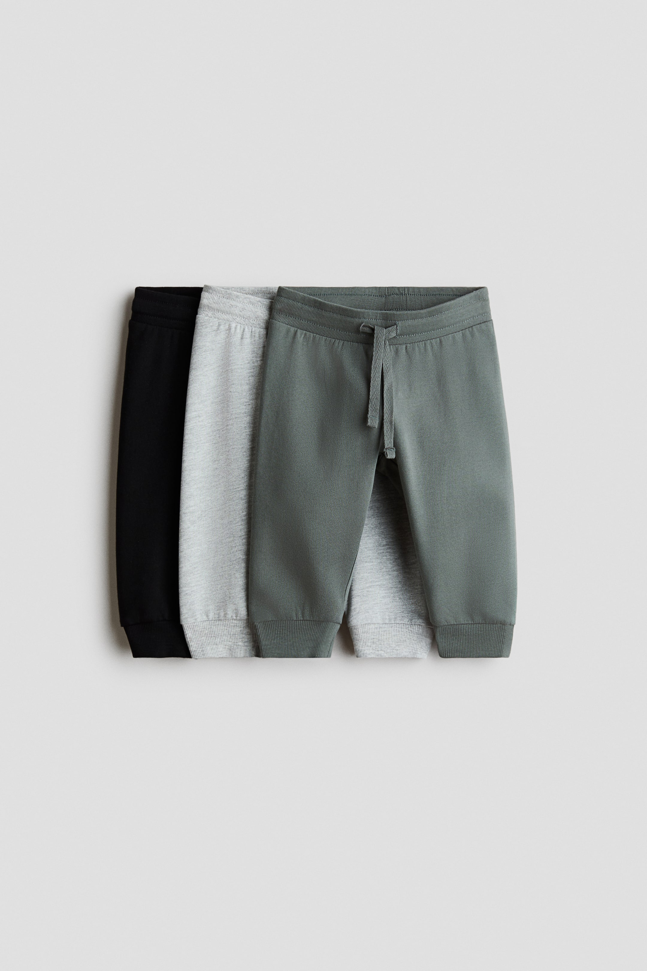 View larger image: Three pairs of joggers are showcased from a front angle, featuring a green, light grey, and black pair layered together. Each jogger displays a sweatshirt fabric, an elasticated ribbed waistband with a drawstring, and ribbed hems.