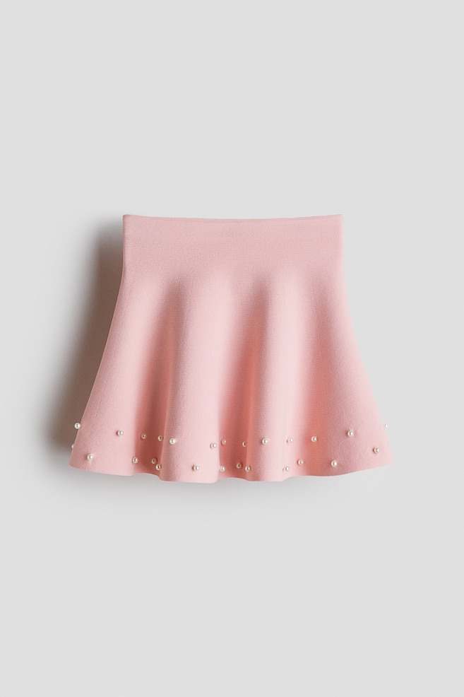 A light pink A-line mini skirt is presenting from the FRONT, featuring a structured waist and small, round pearl embellishments scattered along its flared hemline. - 1