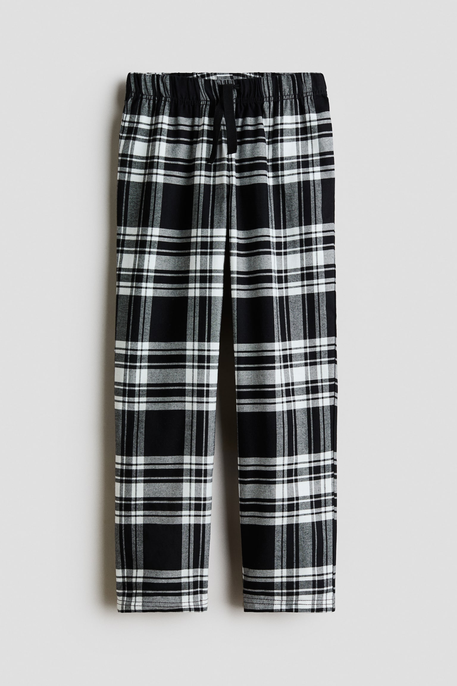 Pyjama pants in a black and white plaid pattern are shown from the front, featuring straight-cut legs. The pants are designed with a gathered elastic waistband and a black drawstring tied at the center.