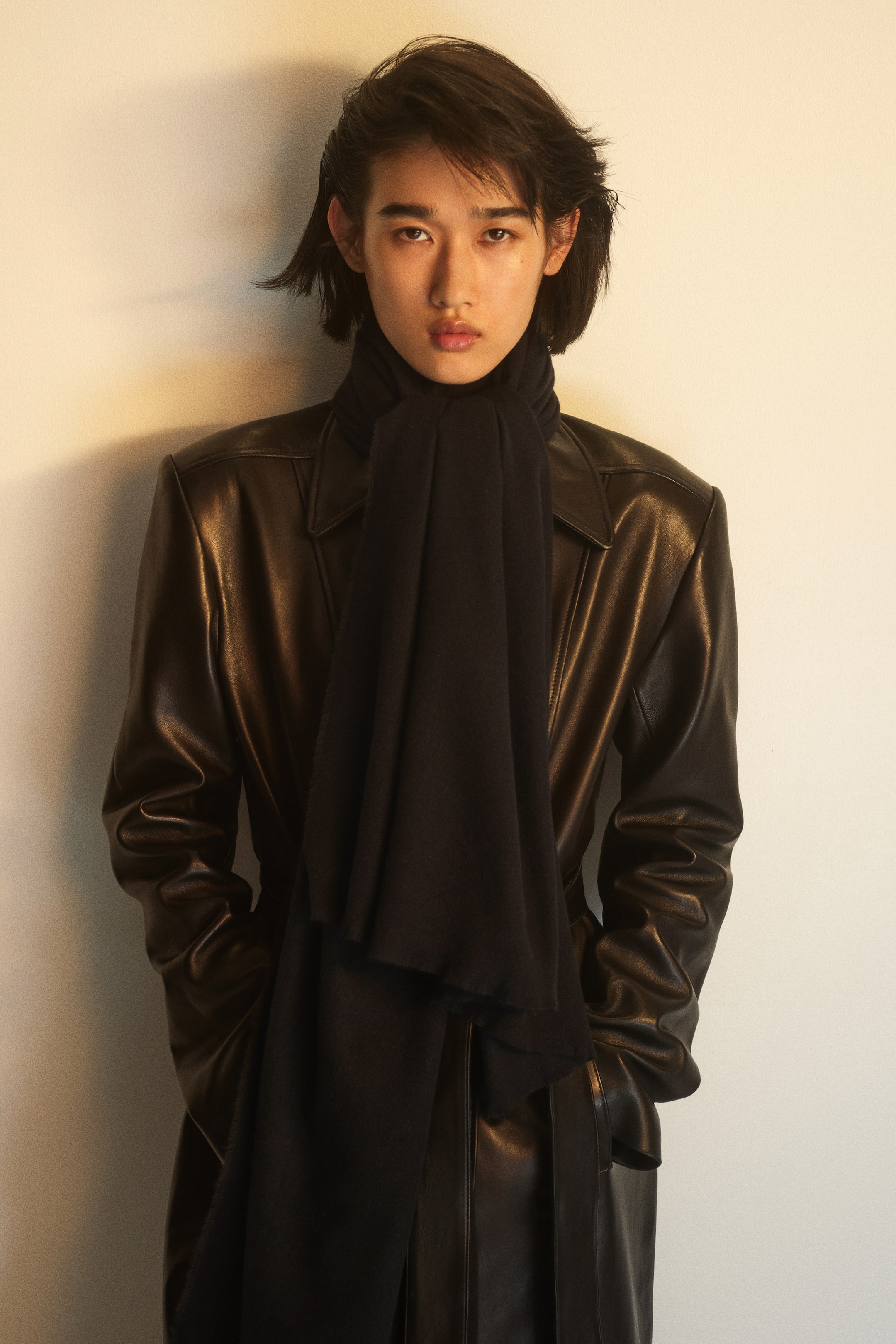 View larger image: A black blanket scarf in a soft weave with frayed edges is being worn by the model, wrapped around the neck with its long ends draped down the front of a dark leather coat.