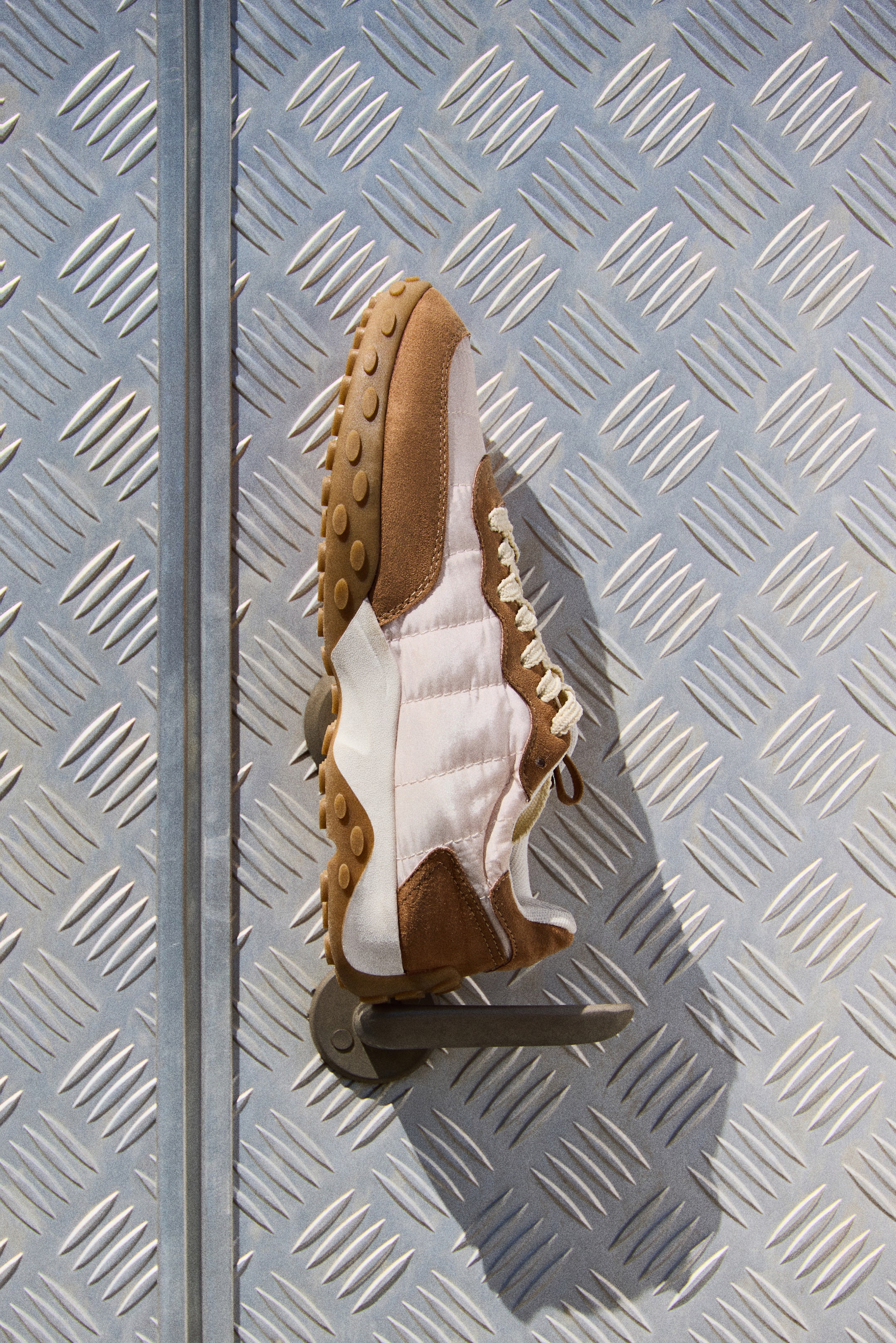 Visualizza immagine più grande: Una sneaker a basso profilo è presentata in vista laterale, caratterizzata da nylon trapuntato rosa chiaro e tessuto marrone scamosciato. Presenta lacci color crema sul davanti, un bordo imbottito e una suola in gomma marrone spessa con un motivo sul lato inferiore.