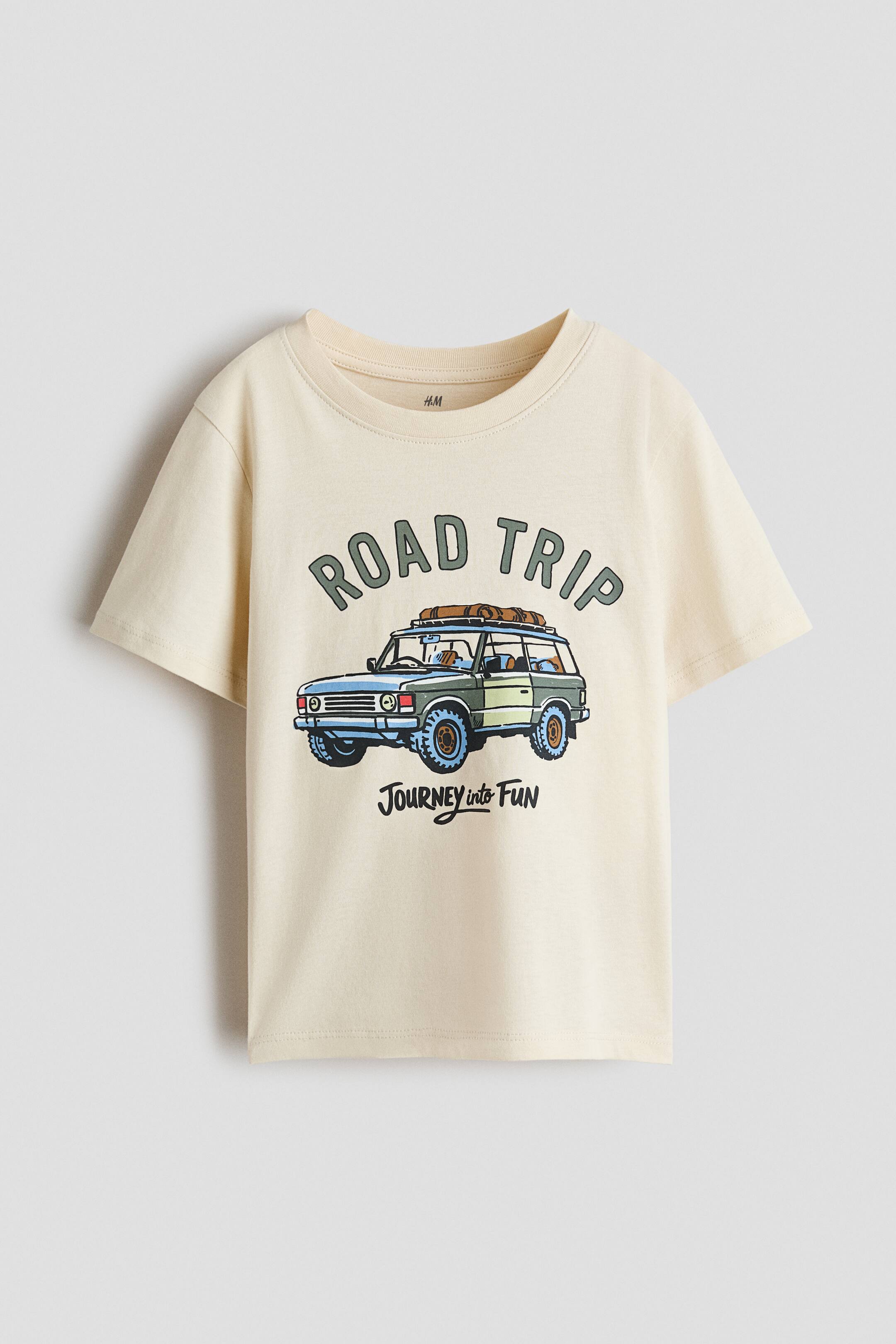 View larger image: A T-shirt in printed cotton jersey is shown from the front, featuring a ribbed crew neckline and softly dropped shoulders. The front showcases a graphic print with the text "ROAD TRIP," an off-road vehicle, and the text "Journey into Fun".
