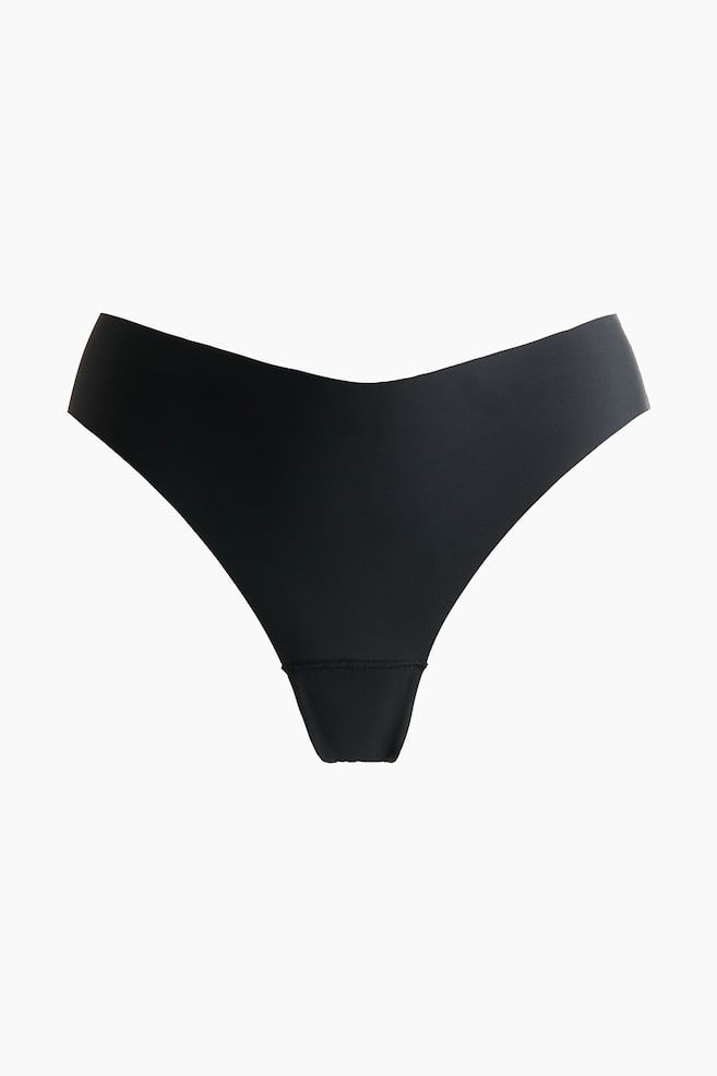 A black thong is displaying a seamless design with a V-shaped front waistband. - 1