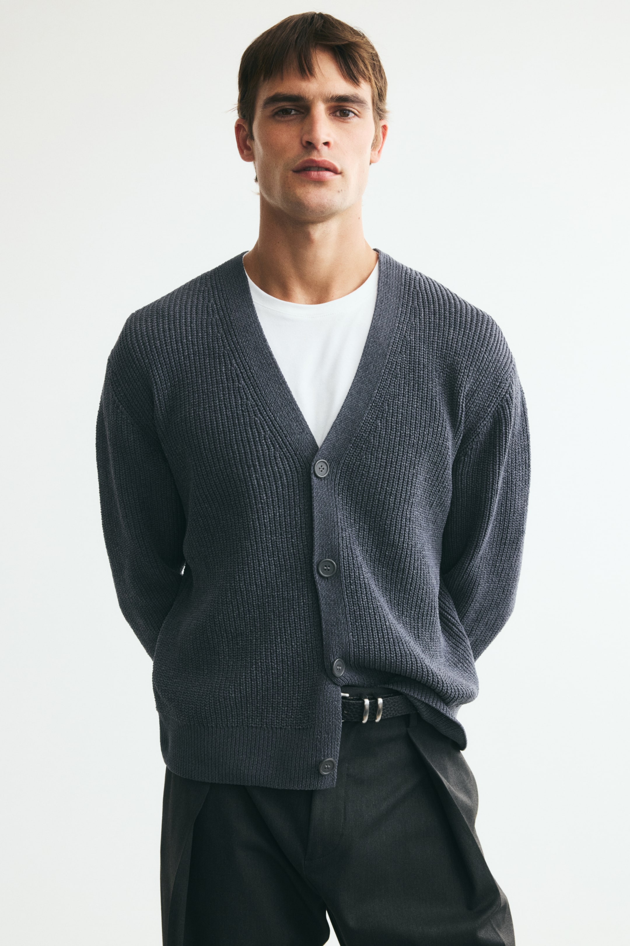 View larger image: A dark grey rib-knit cardigan is being worn by the model, featuring a V-neckline and front button closure. It is partially buttoned over a white T-shirt, with a relaxed fit and ribbed cuffs and hem.
