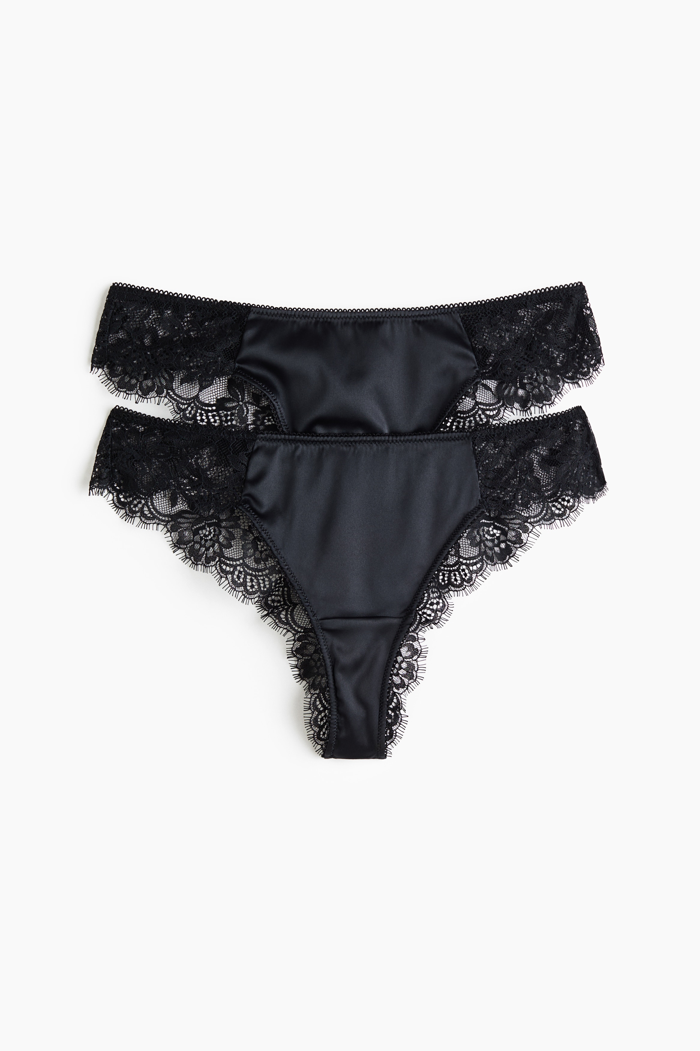 Una modelo lleva una braguita de satén negro y encaje con cintura baja y delicado ribete de encaje. La braguita se combina con un bralette a juego de satén negro y encaje.