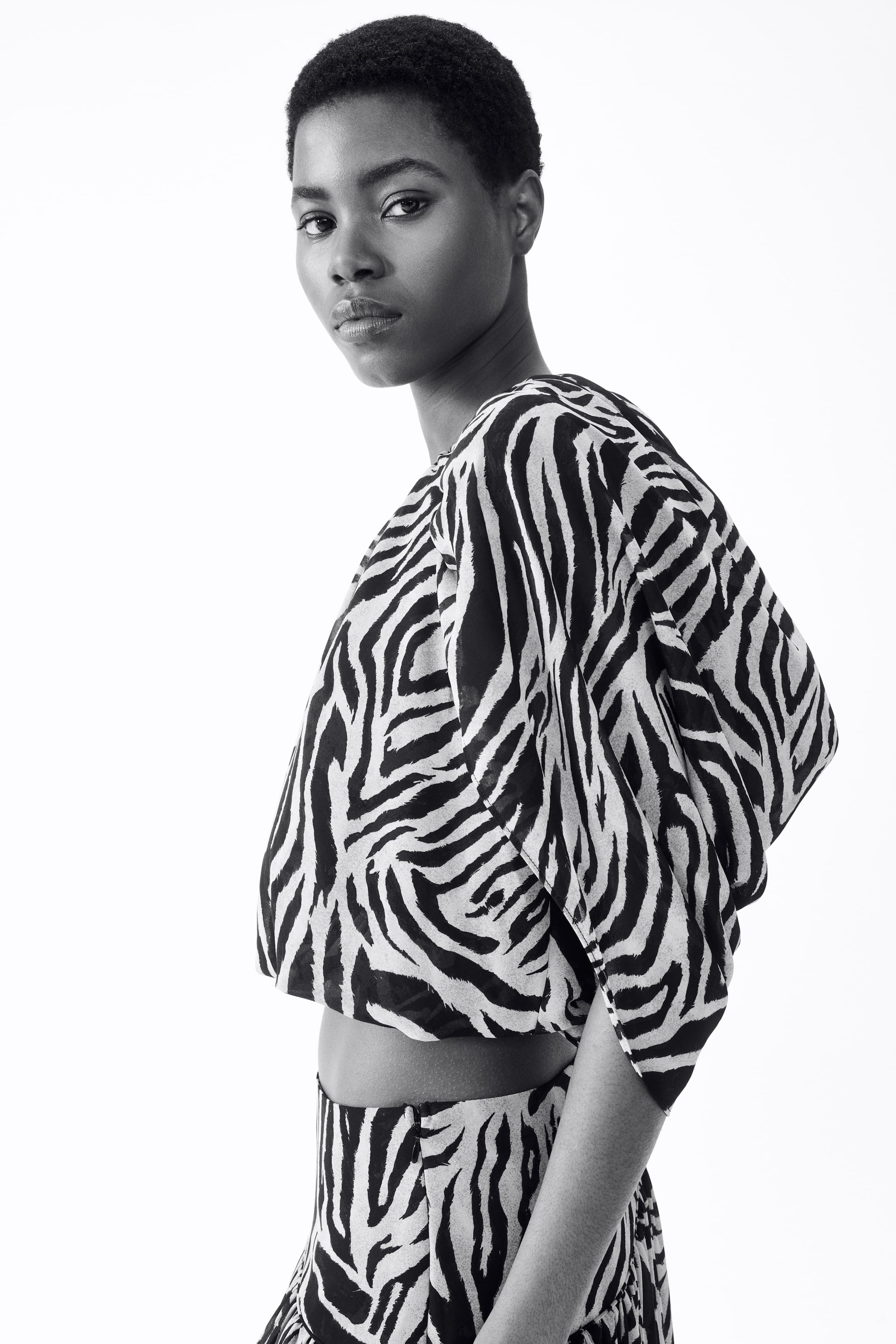 Größeres Bild ansehen: Ein schwarz-weißes Zebra-Print-Crop-Top wird zusammen mit einem passenden Unterteil getragen. Das Top ist locker geschnitten, hat weite kurze Ärmel und ist bauchfrei, wodurch die Taille freigelegt und das passende Bündchen des Unterteils betont wird.