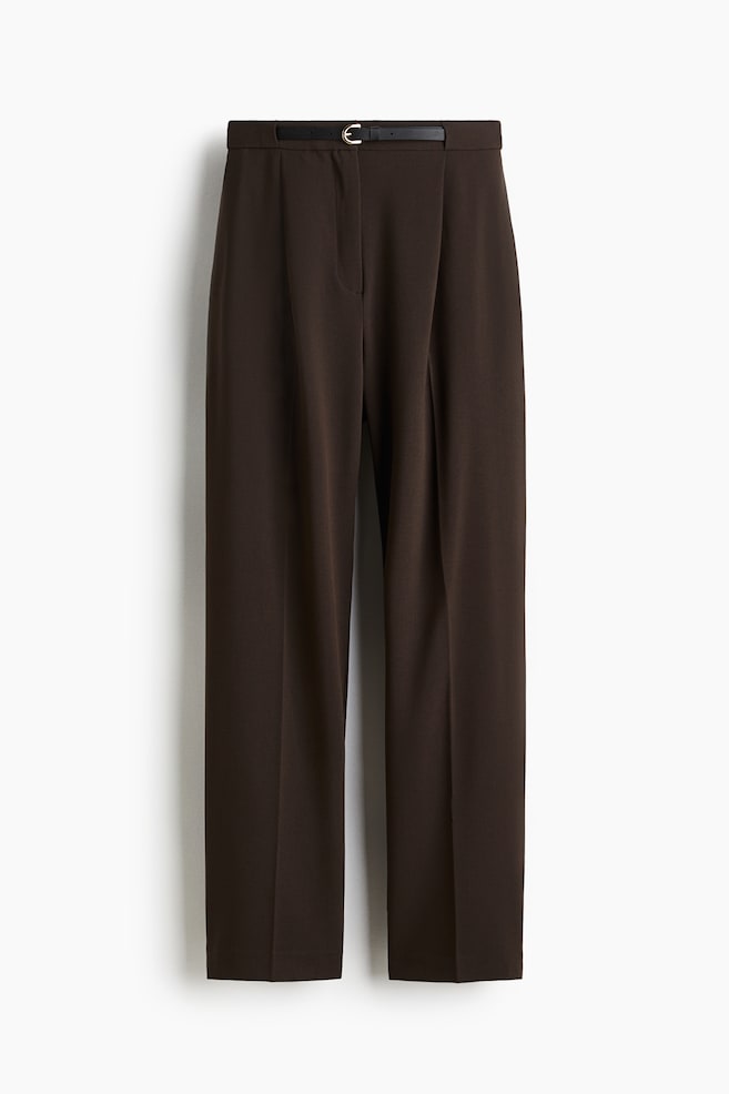 A pair of dark brown trousers is hanging, presented from the front. They are featuring a flat waistband with belt loops and a thin black belt with a gold-tone buckle. A concealed zip fly is closing the front, and single forward-facing pleats are detailing each leg. - 1