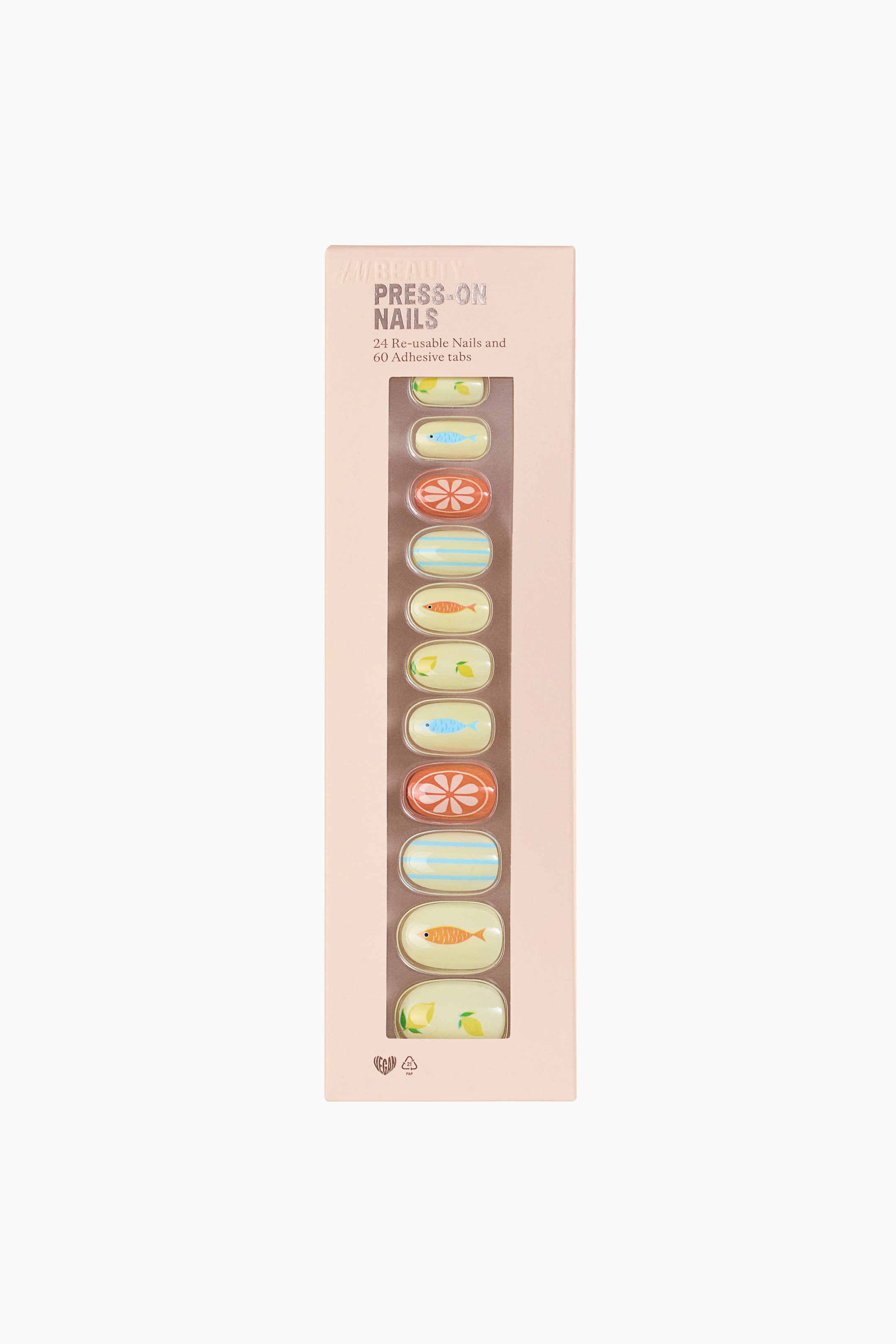 View larger image: A light pink rectangular box of press-on nails is displayed at the front. A clear vertical window on the box showcases multiple oval-shaped nails, featuring alternating designs of yellow lemons, blue fish, orange citrus slices, blue stripes, and orange fish. The box also displays the text 'H&M BEAUTY PRESS-ON NAILS' and '24 Re-usable Nails and 60 Adhesive tabs'.