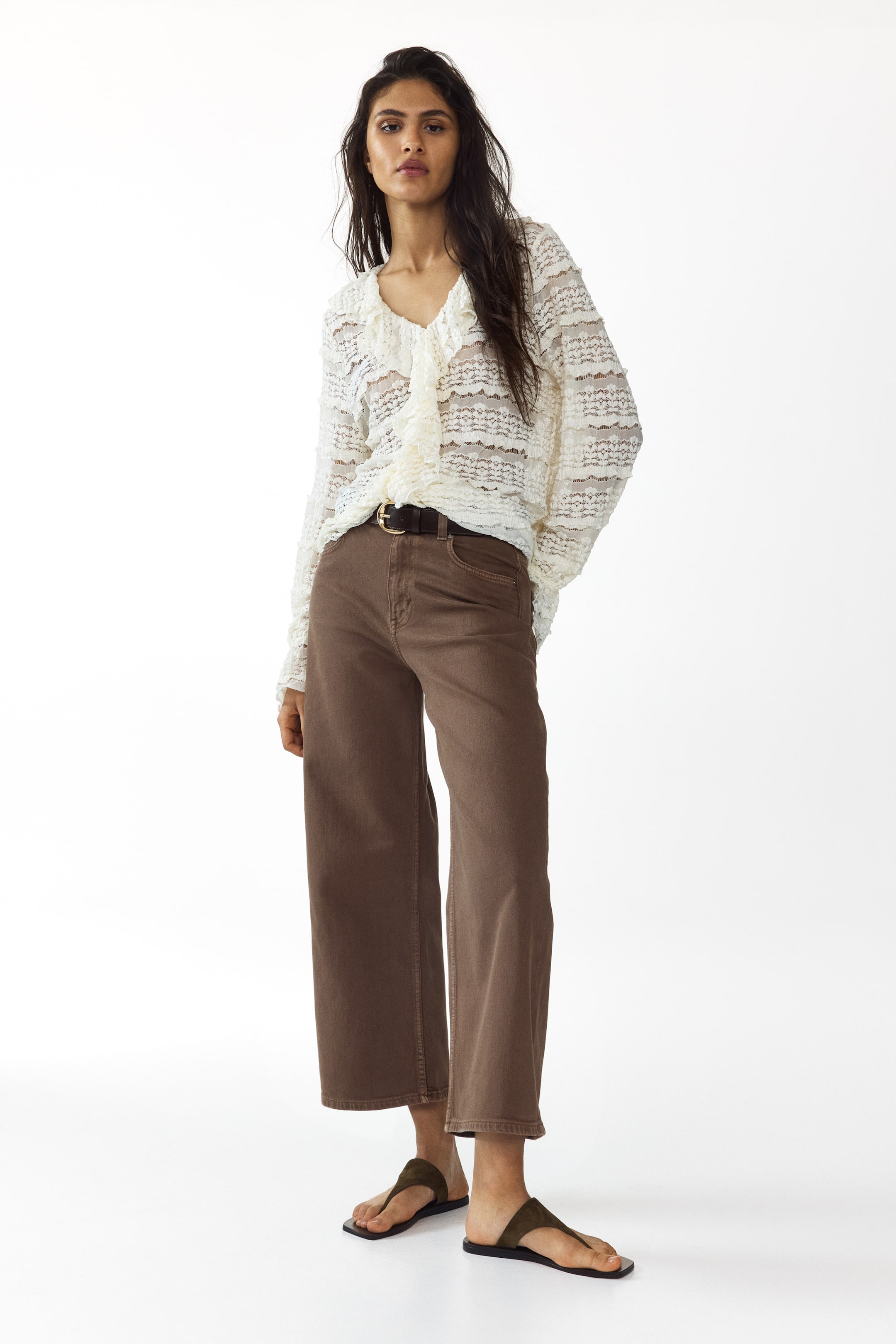 View larger image: The model is wearing brown denim 5-pocket jeans, featuring a high waist with button closure. These jeans showcase a wide leg with a regular fit through the hip, extending into a wide cut from the thigh to the ankle-length hem. A dark brown belt cinches the waist, adding a stylish touch to the ensemble.