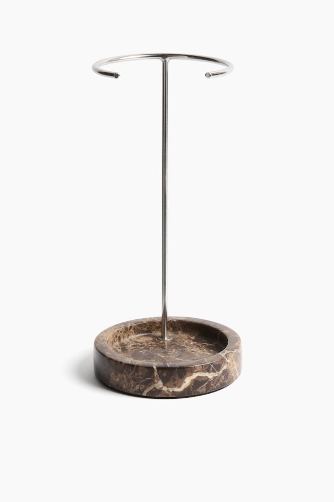 A display stand featuring a round, brown marble base with white veining, from which a silver-coloured metallic rod rises, supporting a circular metallic ring at the top. - 1