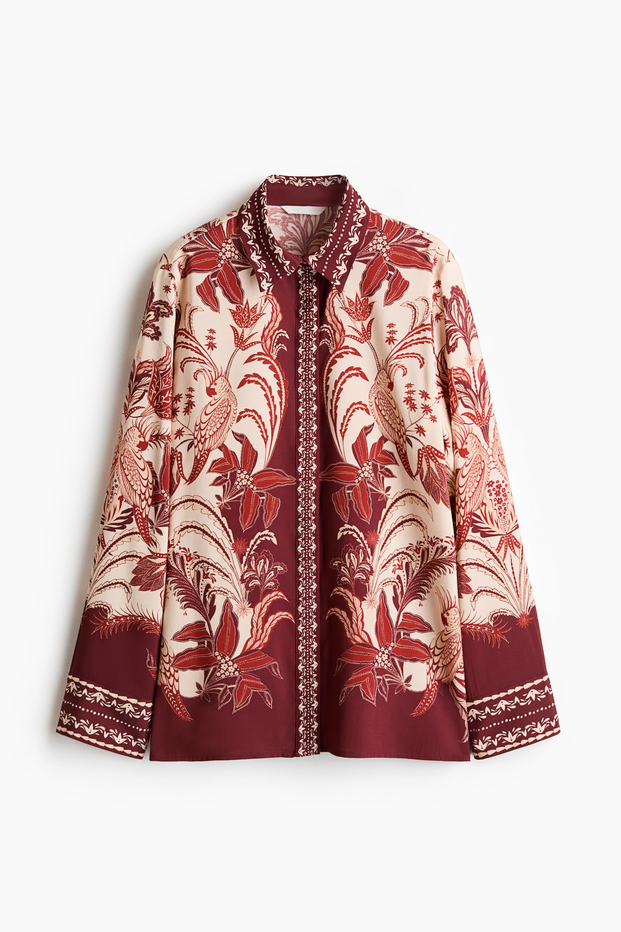 View larger image: The front view of an oversized shirt is displayed, showcasing an intricate red and cream botanical and bird motif with a central vertical band and border designs. It comes with a collar, a concealed button placket, long sleeves with buttoned cuffs, and a straight-cut hem.