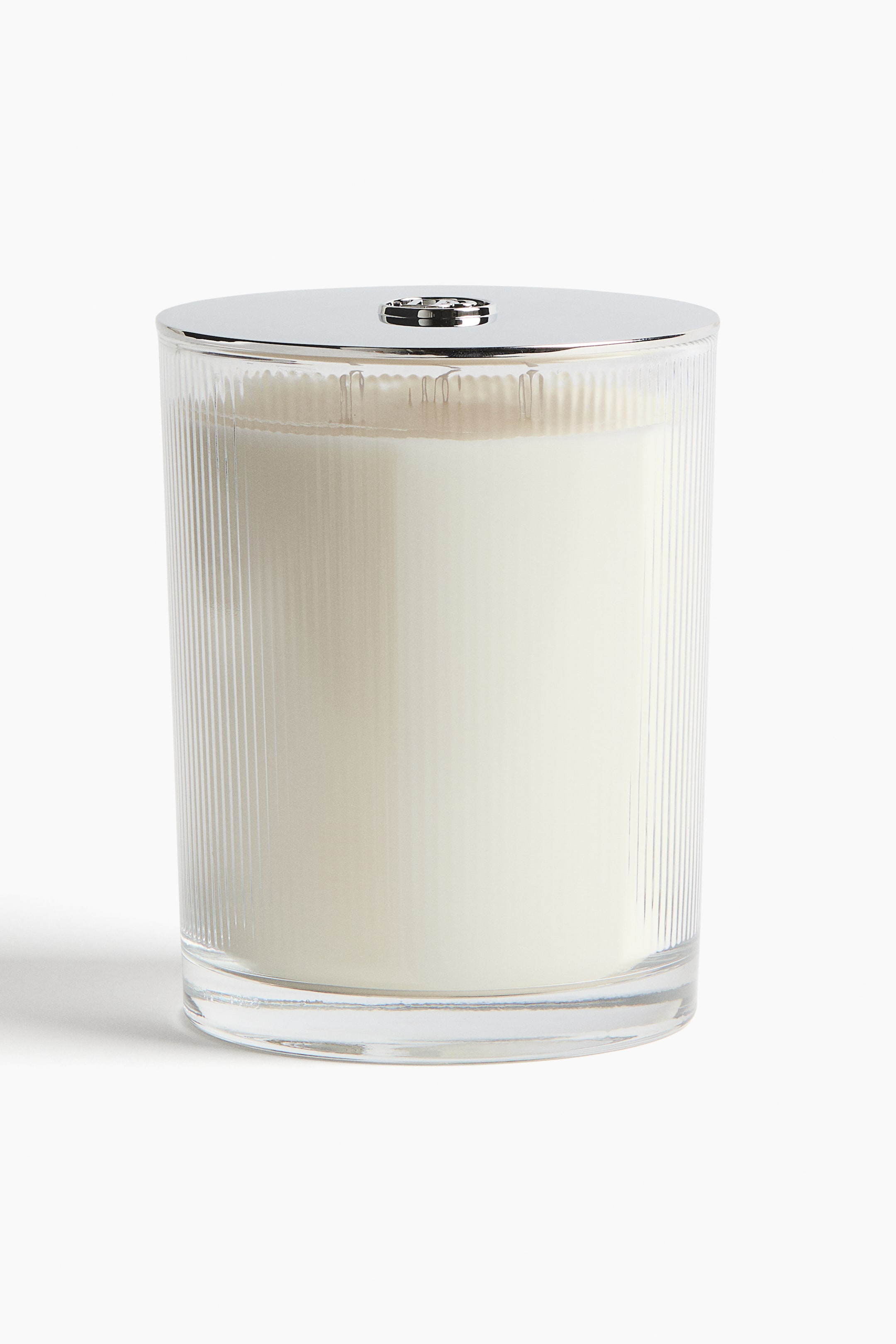 Ver imagem maior: Mostrando uma vista frontal, uma vela num recipiente de vidro transparente com estrias verticais está em posição vertical, exibindo cera de cor creme no interior. O recipiente é rematado por uma tampa plana, polida, de tom prateado, com um pequeno botão central.