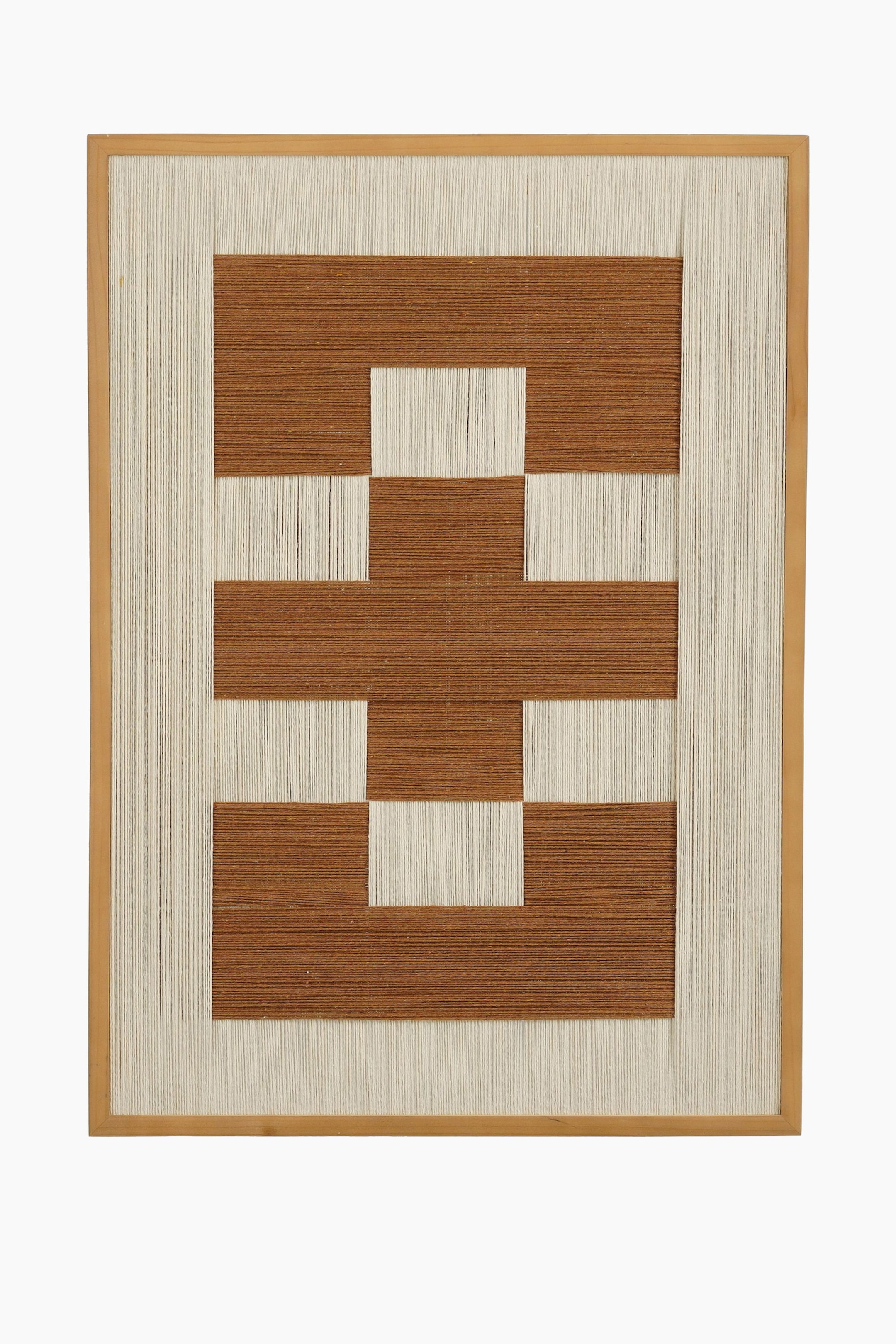 Größeres Bild ansehen: Ein rechteckiges Textilkunstwerk wird in einem hellbraunen Holzrahmen präsentiert und zeigt cremefarbene und rötlich-braune Fäden. Die Fäden formen ein geometrisches Muster aus ineinandergreifenden Rechtecken, wobei die cremefarbenen Fäden einen Rand um das zentrale Design bilden.