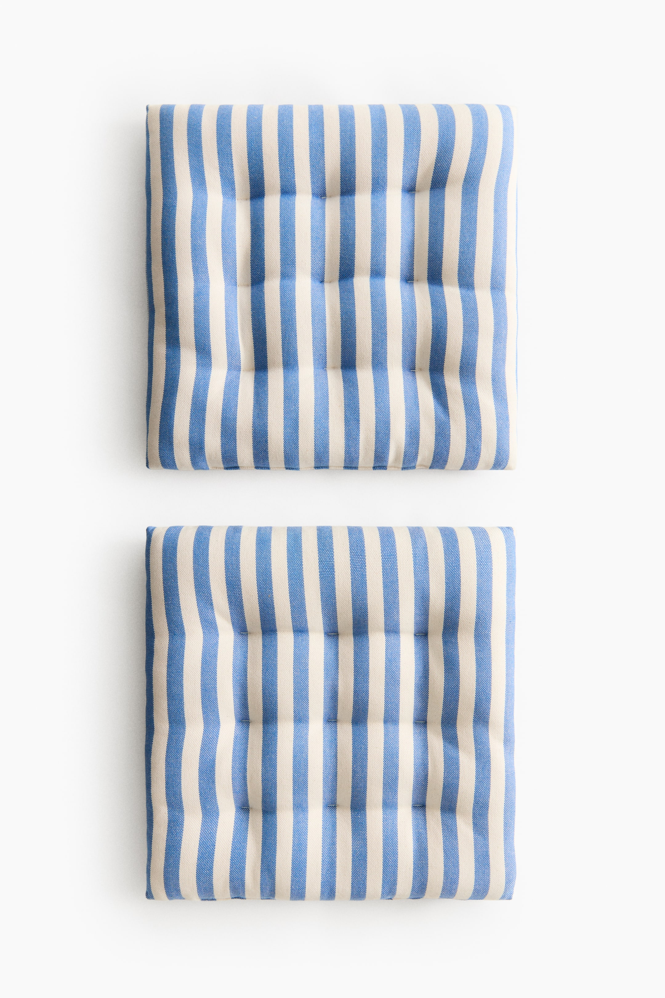 View larger image: Two square, padded seat cushions show their fronts, featuring alternating blue and off-white vertical stripes. Visible quilt knots indent the woven fabric, helping the cushions retain their padded shape.