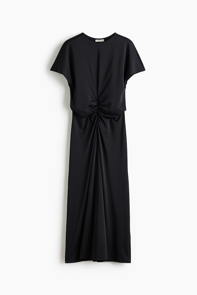The black dress features a round neck and short, loose sleeves, crafted from a satin-like fabric. It showcases prominent ruching at the centre front, cinching the waist and flowing into a long, draped skirt. - 1