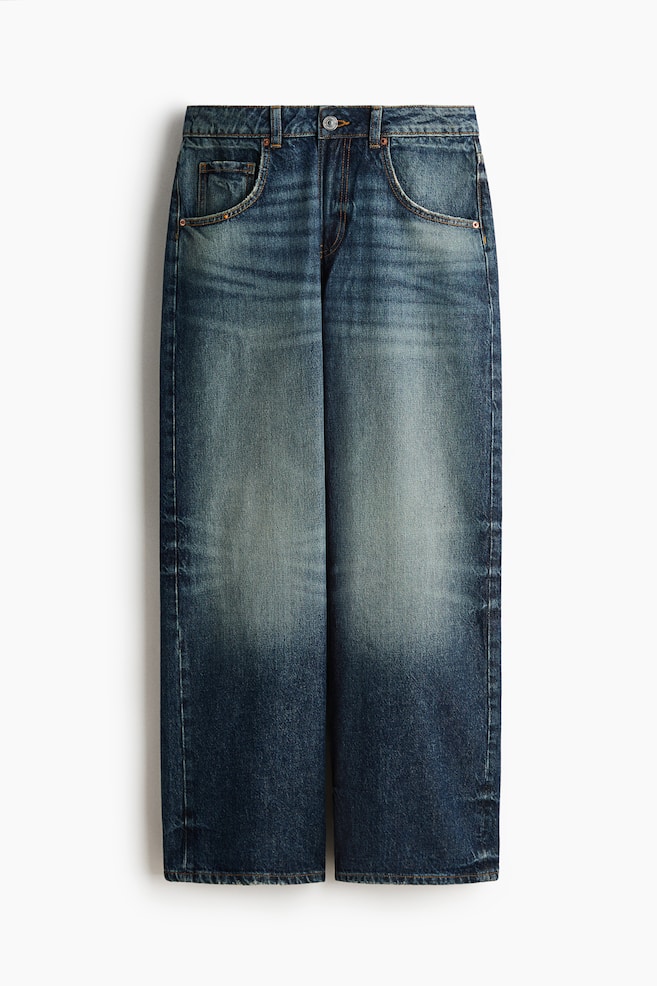 Jeans en denim bleu posés à plat en vue de face, arborant un délavage usé avec des zones plus claires sur les cuisses et les genoux. Ils présentent une fermeture à bouton métallique unique, des passants de ceinture à la taille, deux poches avant incurvées avec de petits rivets métalliques, et des jambes droites avec un ourlet standard. - 1