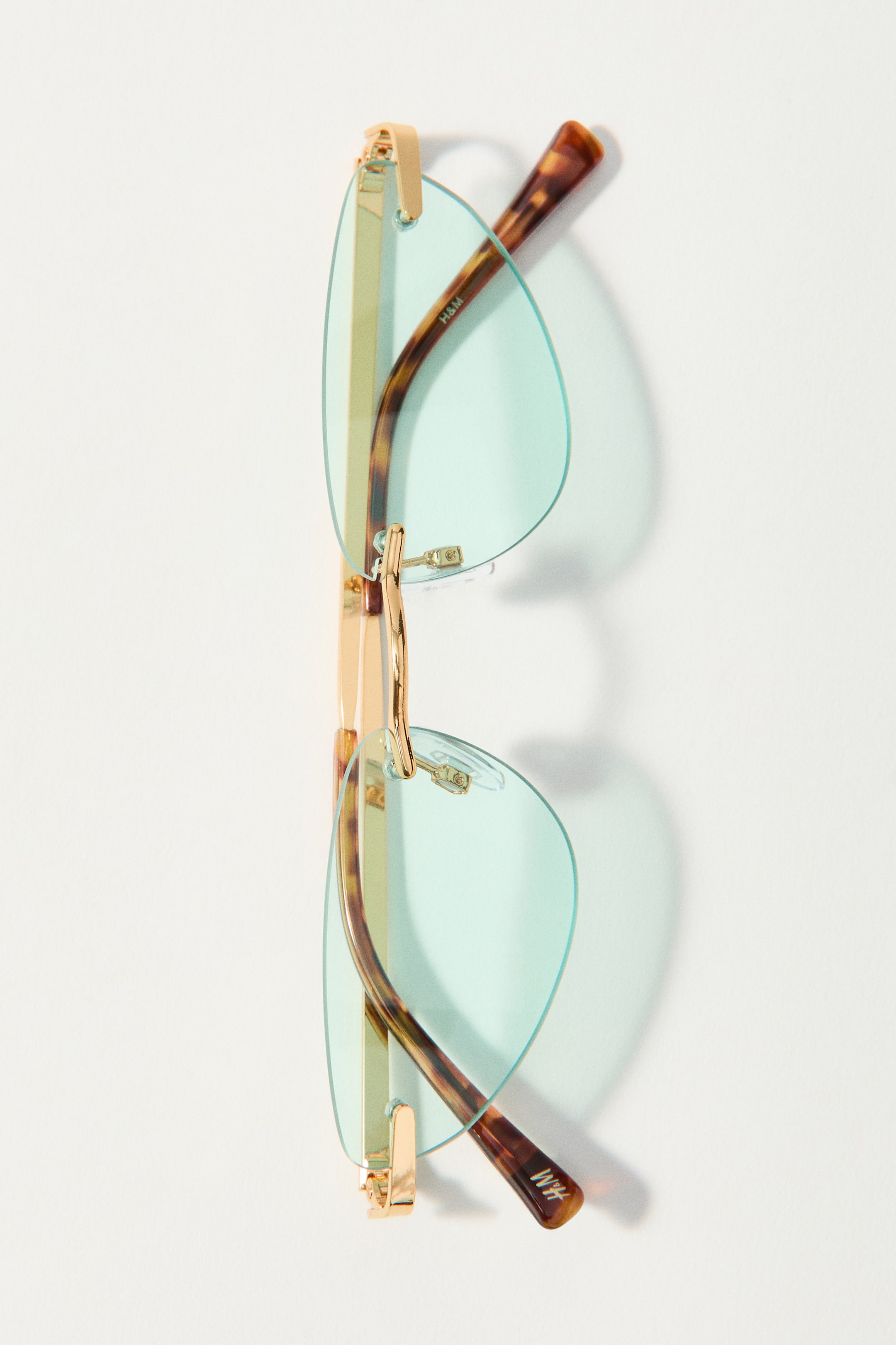 Grösseres Bild ansehen: Randlose Cat-Eye-Sonnenbrillen mit hellgrün getönten Gläsern, goldfarbenen Bügeln und verstellbaren transparenten Nasenpads, mit Schildpatt-Bügelenden.