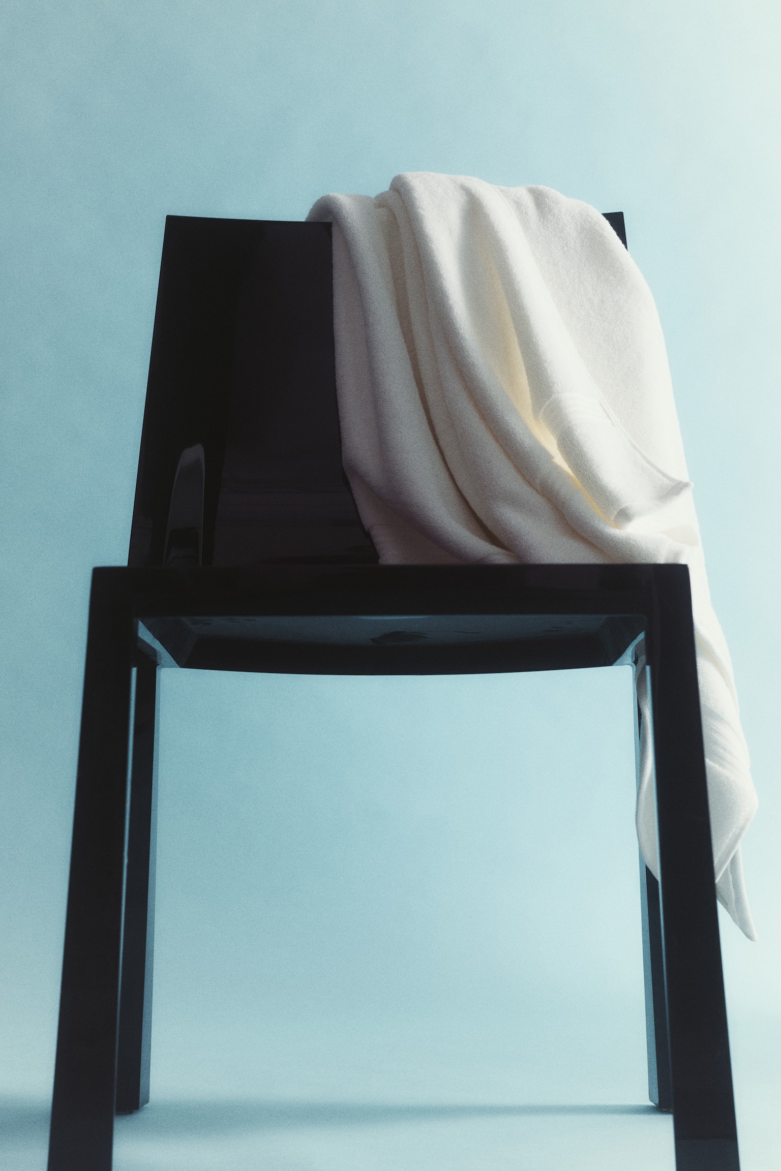 An off-white towel is folded in half lengthwise, draping over a black hook and displaying subtle textured bands near its bottom edge. - 1