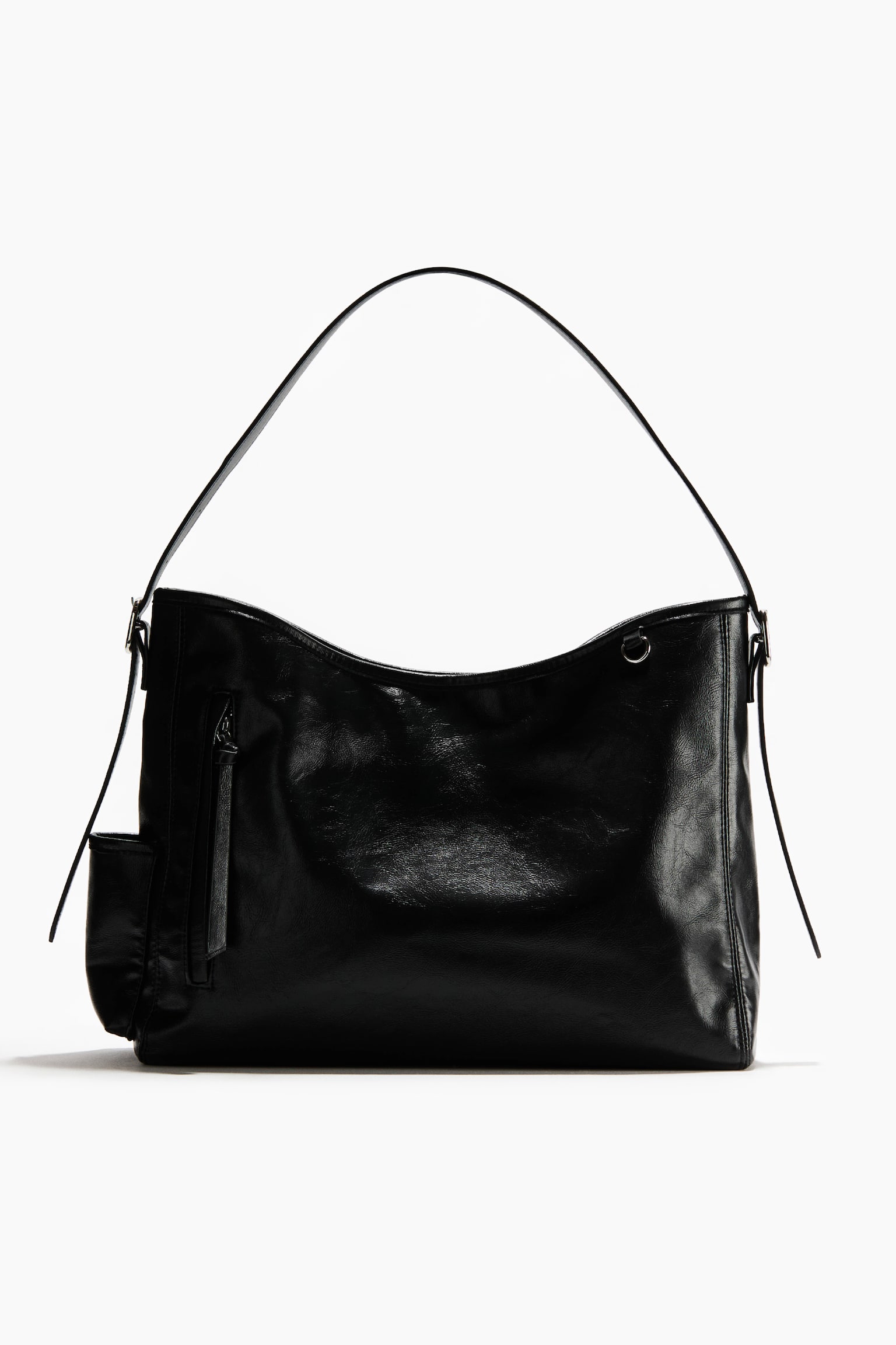 Un bolso de hombro de cuero negro está de pie en posición vertical y de frente, mostrando un acabado brillante y texturizado. Una sola correa plana para el hombro se arquea sobre la parte superior curvada, y un bolsillo vertical con cierre y una lengüeta larga de tiro detalla el lado frontal izquierdo.