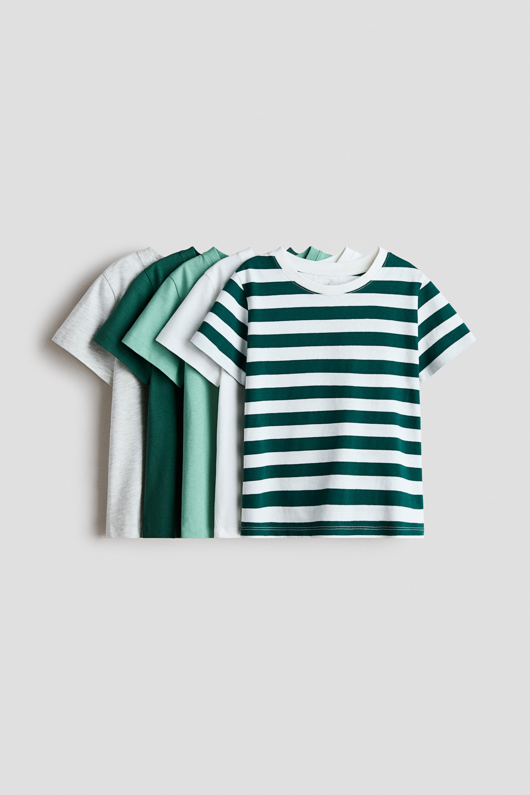 Ver imagen más grande: Camisetas de suave punto de algodón con cuello redondo y dobladillo recto están mostrando sus frentes. Se ven cinco camisetas, que comprenden una con rayas verde oscuro y blanco, una blanca sólida, una verde claro sólida, una verde oscuro sólida y una gris claro sólida.