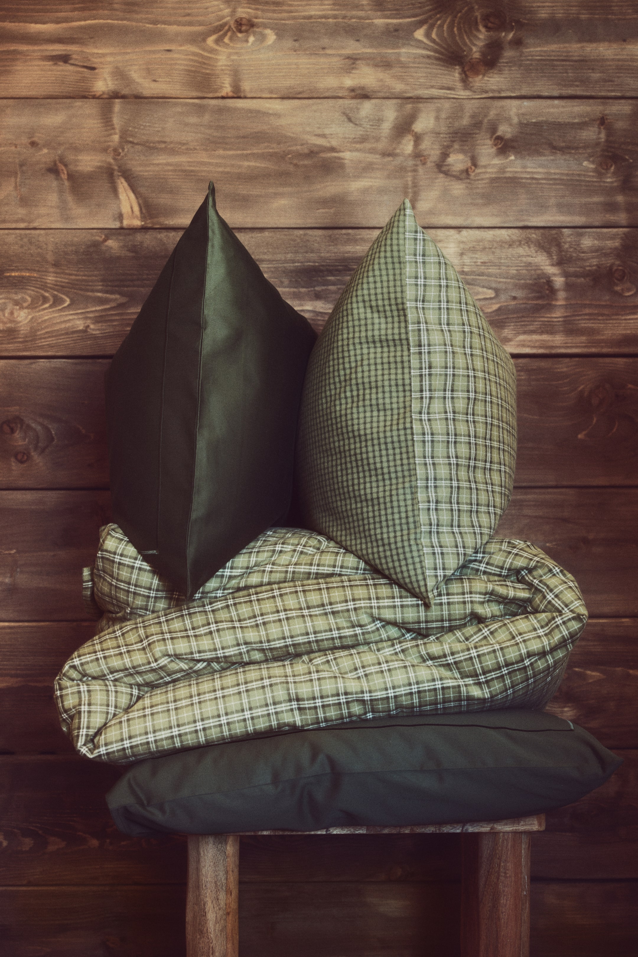 View larger image: A cotton flannel quilt cover set is displayed, featuring a folded quilt cover in a green-and-white yarn-dyed check pattern. The set is shown with two upright pillows—one solid dark green and one featuring a reversible design with two coordinating green check patterns—resting on the folded quilt, which sits atop another solid dark green pillow.