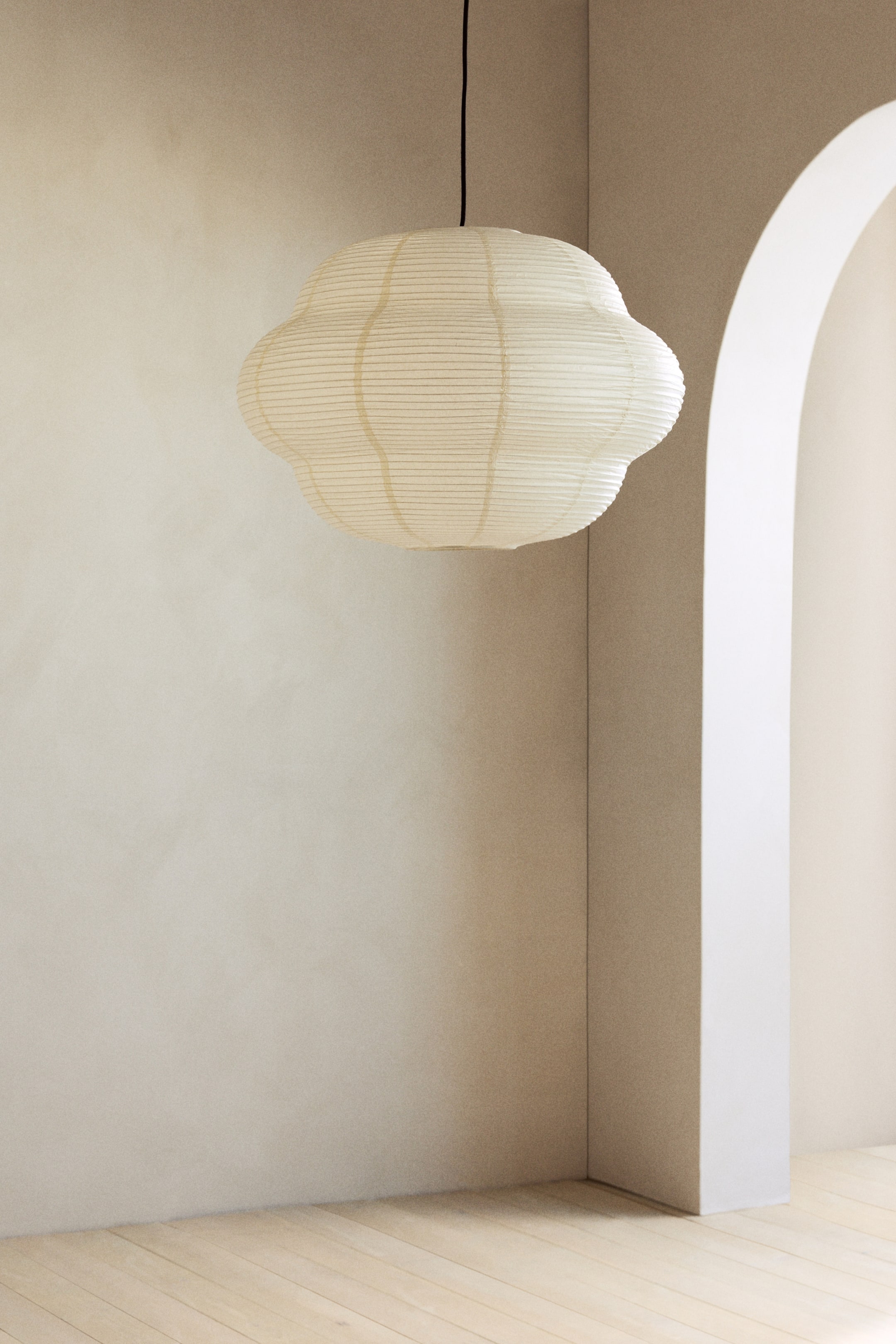 Agrandir l'image: Une suspension en forme de nuage est suspendue à un cordon noir, orientée vers l'avant. Elle présente un abat-jour translucide de couleur blanc cassé avec des lignes horizontales nervurées et des éléments structurels internes subtils visibles à travers le matériau.