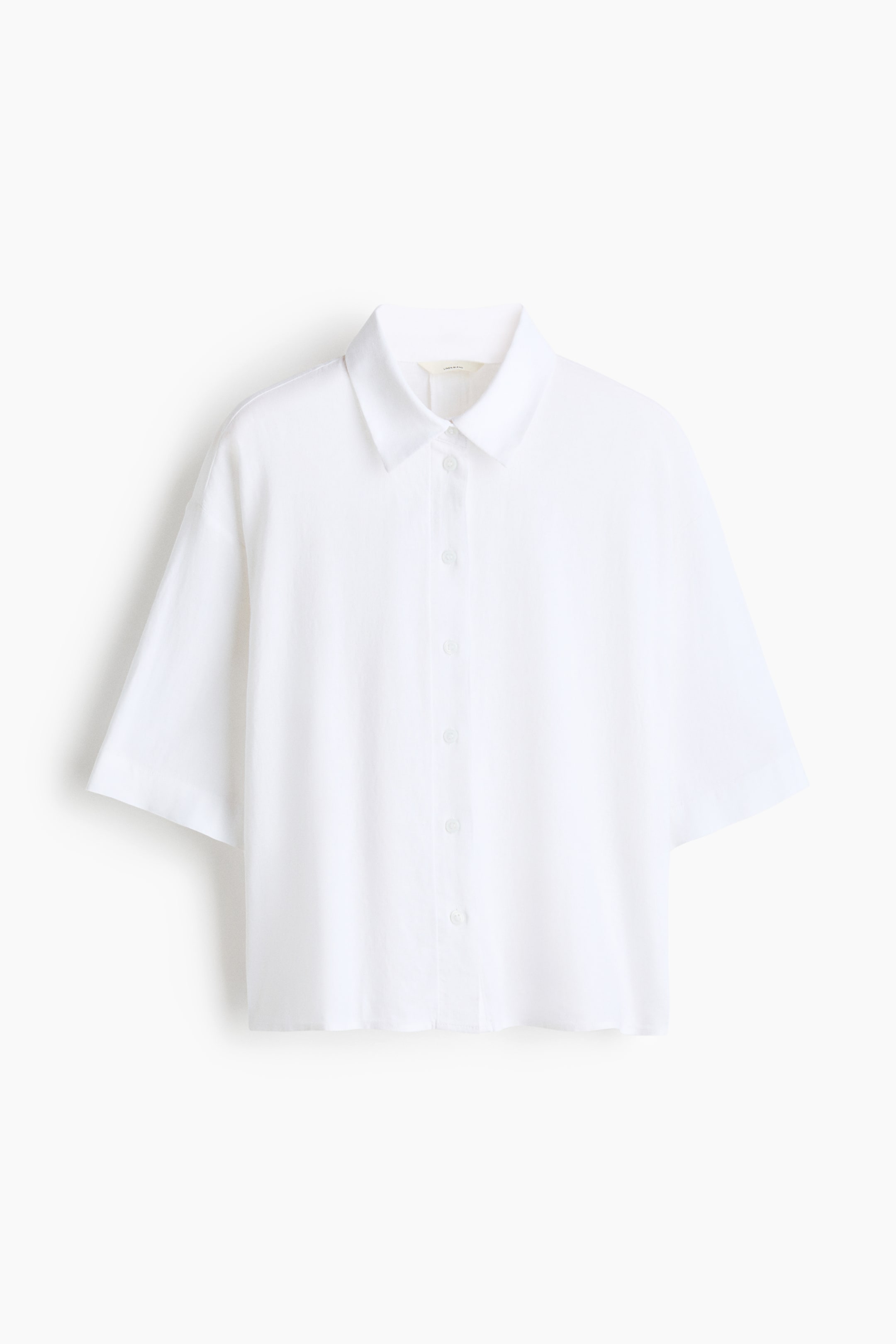 View larger image: An oversized white shirt is showcased from the front, featuring a collar and buttons down the front. It is crafted with dropped shoulders and elbow-length sleeves, highlighting a subtle airy weave texture.