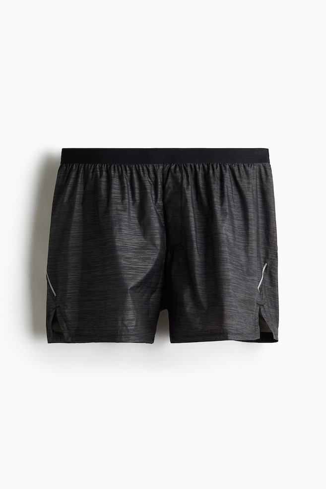A pair of dark grey athletic shorts is being presented from the front, featuring a black elastic waistband, a subtle horizontal striped pattern, and white reflective stripes on each side near the split hems. - 1