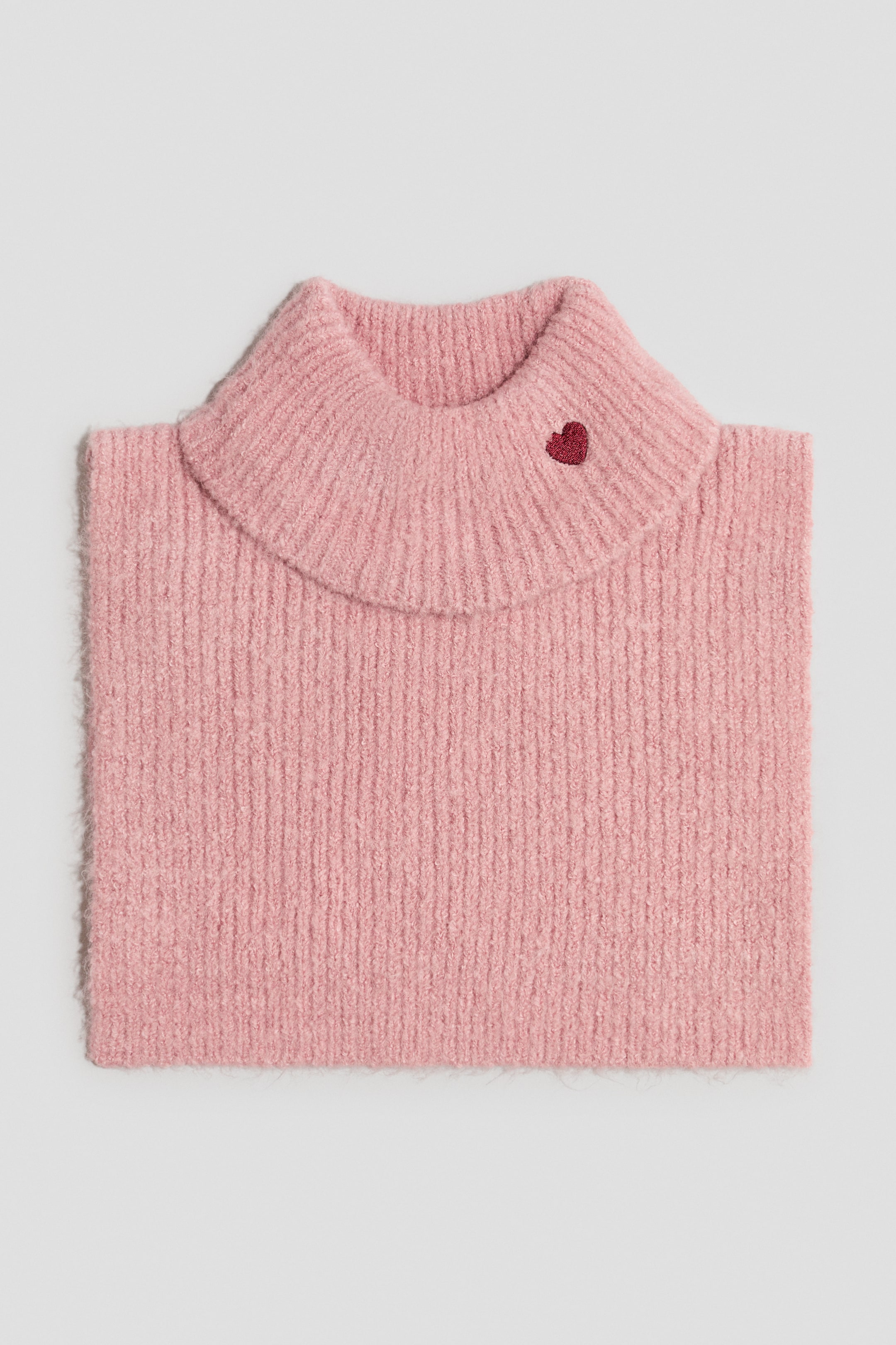 Größeres Bild ansehen: Ein rosa Pullover mit einem breiten, gerippten Kragen und einem kleinen, auf der rechten Seite aufgestickten roten Herz. Der Körper des Pullovers zeigt eine flauschige, vertikal gerippte Strickstruktur.
