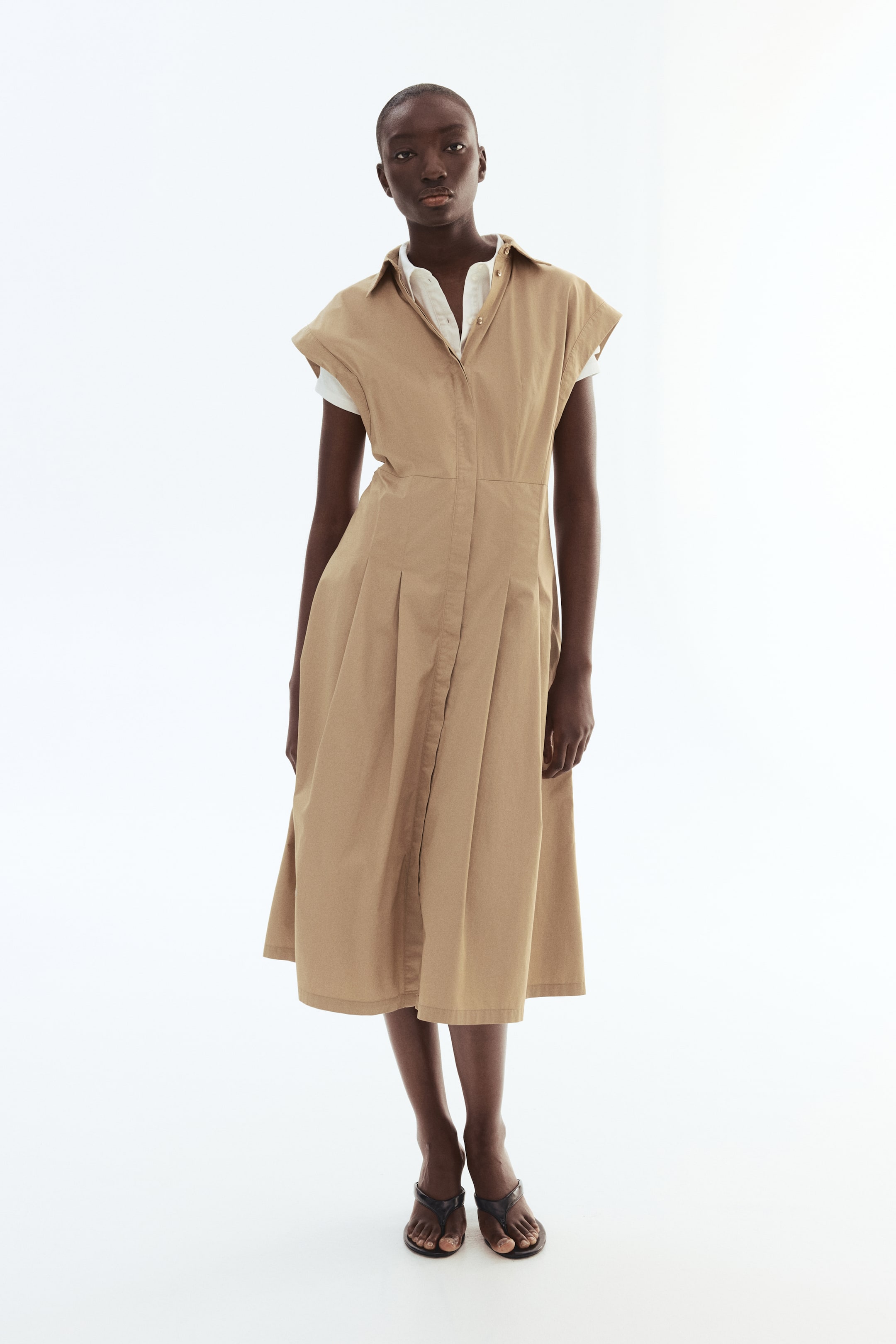 View larger image: The model is donning a beige calf-length dress featuring a collar, a concealed button placket, and cap sleeves. The dress elegantly showcases a gently flared skirt, complemented by a white shirt worn underneath.
