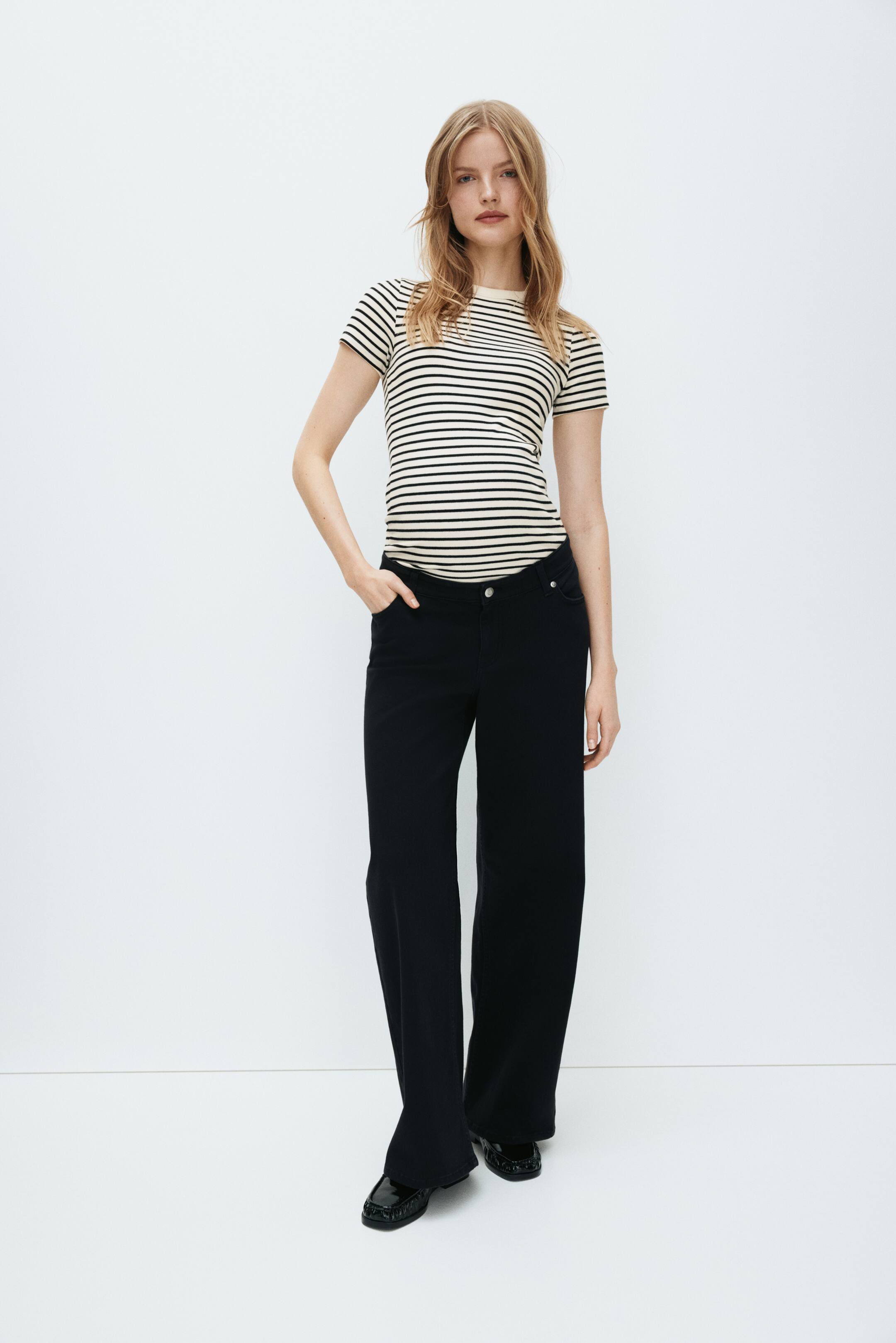 View larger image: A short-sleeve top featuring horizontal dark and light stripes and a round neckline, designed for a close, body-skimming fit. Black wide-leg pants offer a relaxed silhouette, finished with a visible button and pockets at the waist.