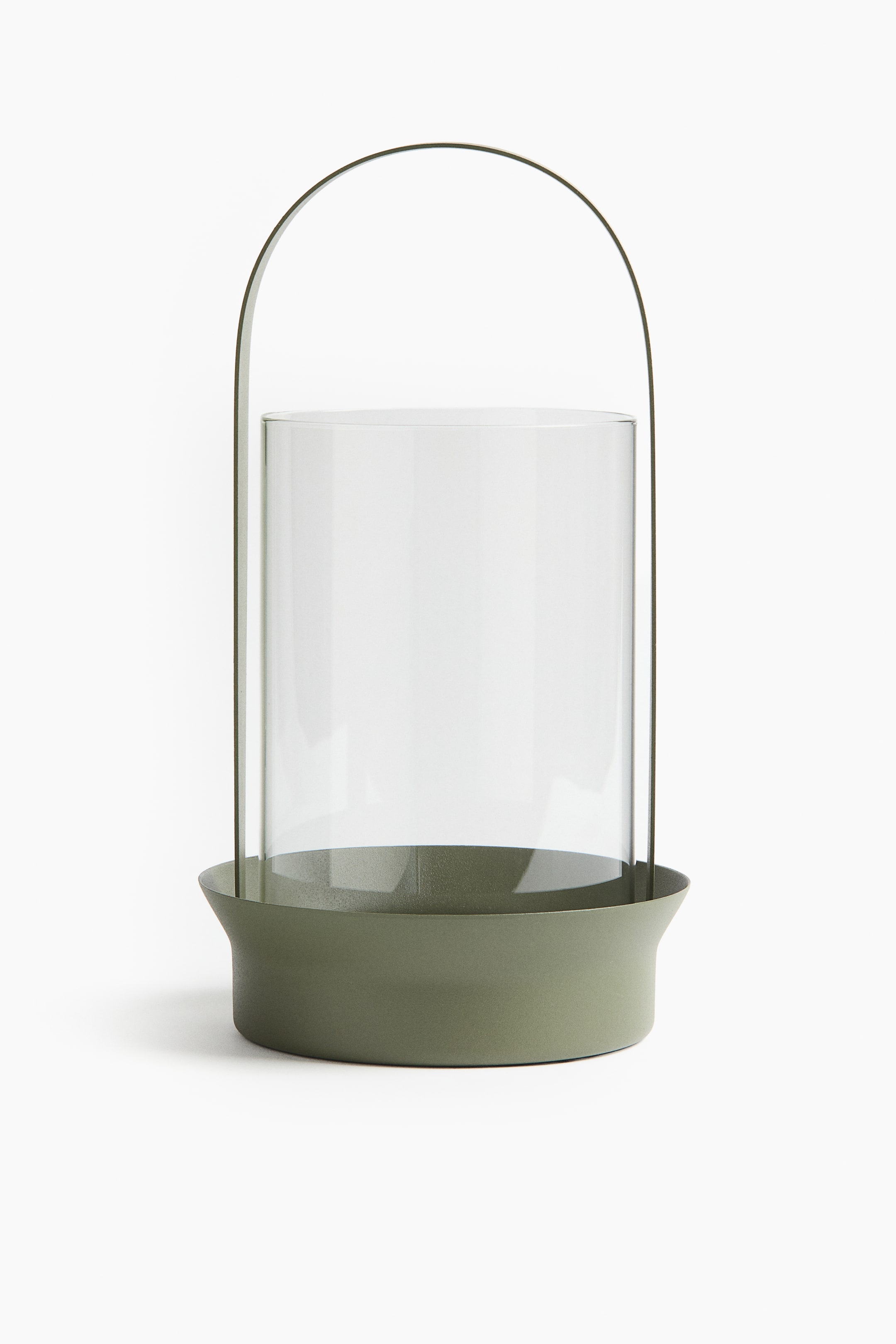 View larger image: A large glass lantern features a clear cylindrical glass enclosure that rests in a wide, matt olive-green metal base. A matching arched metal handle extends from the base, and the lantern is designed to hold a pillar candle.