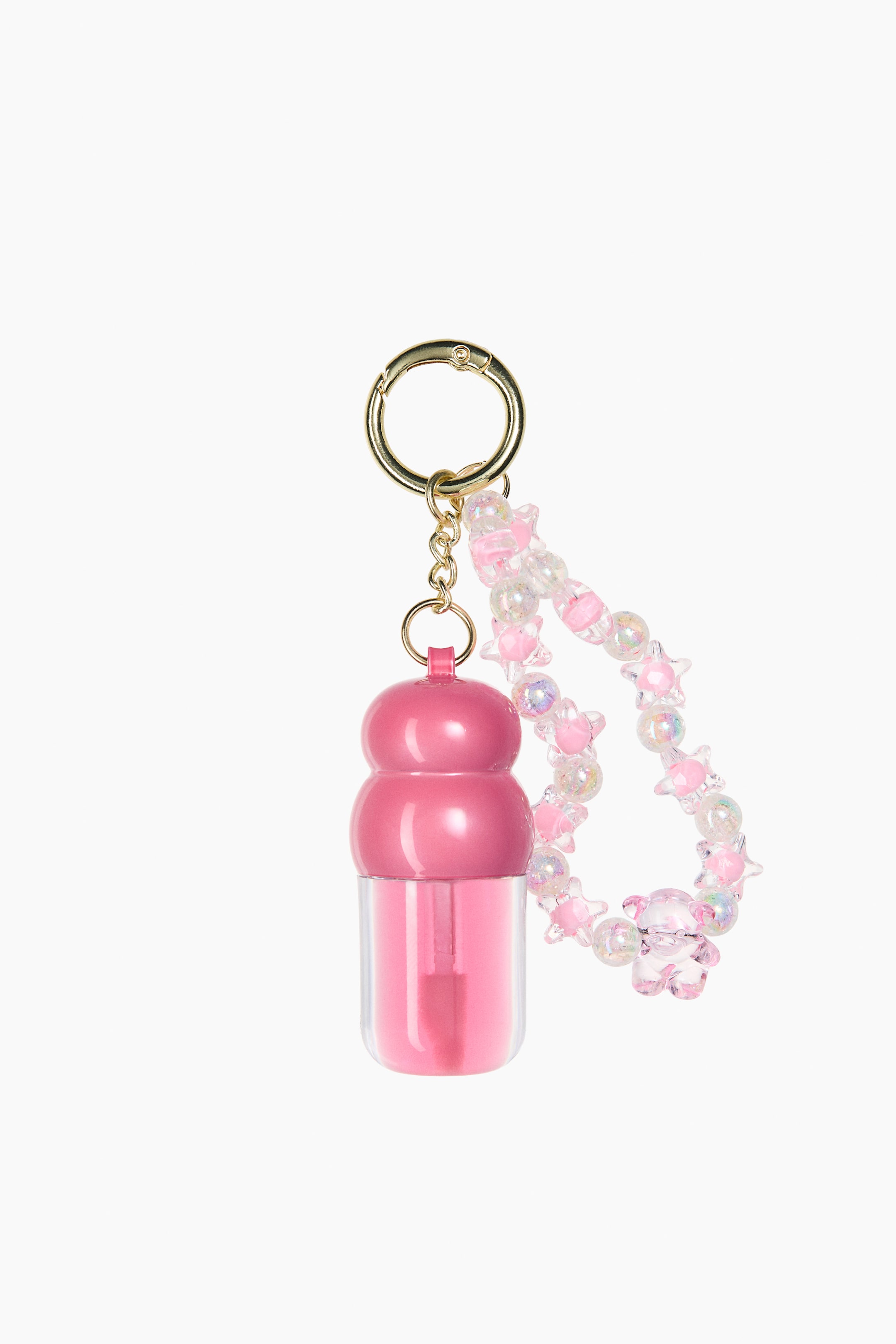 View larger image: A gold-toned keychain holds a mini lip oil, displayed front-facing, with a pink double-sphere cap and a clear body filled with pink liquid. It also holds a looped bracelet adorned with clear, pink, and iridescent plastic beads in various round, star, and bear shapes.