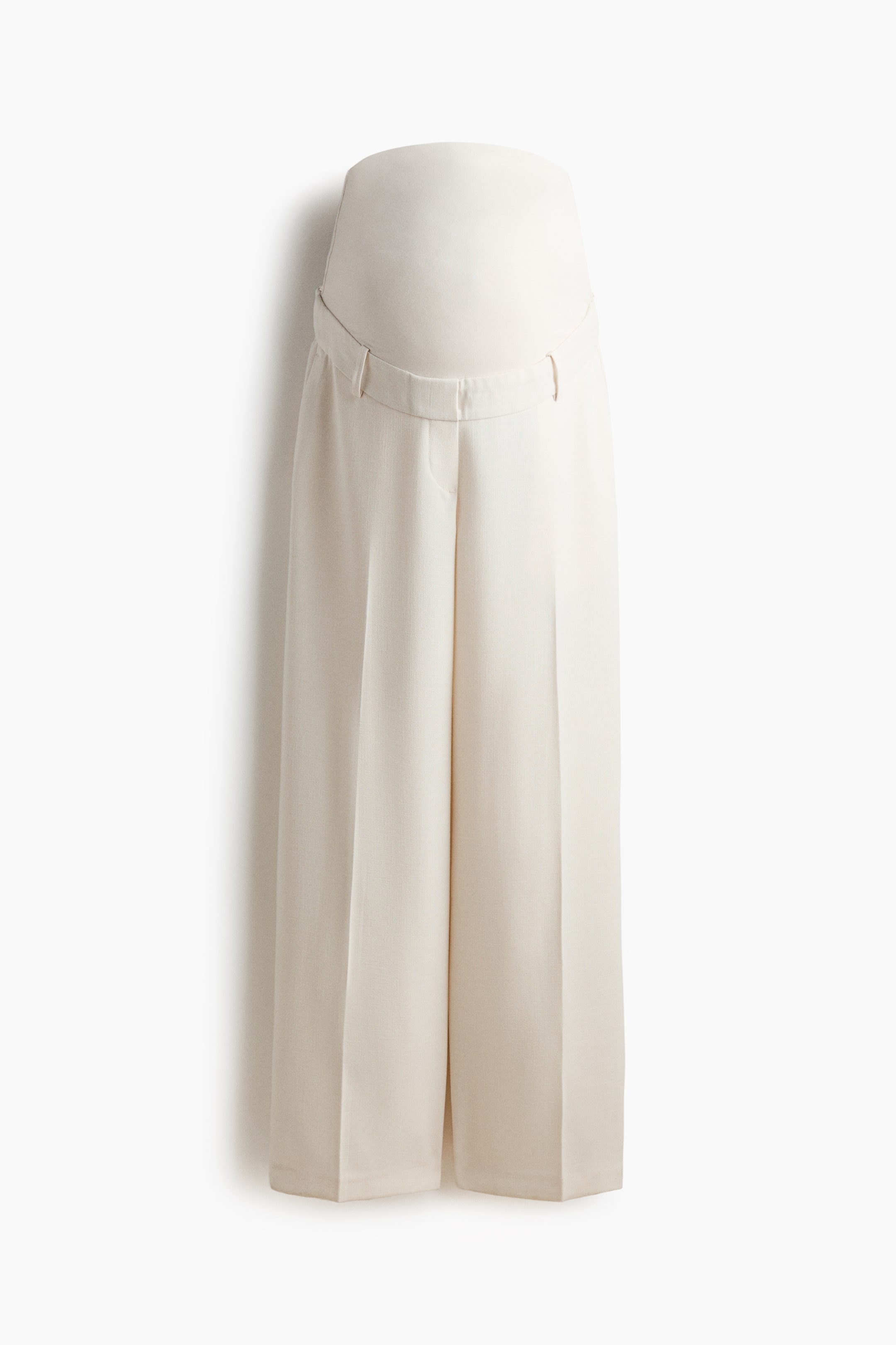View larger image: The tailored trousers are shown from the front, highlighting a wide jersey panel at the waist designed for the tummy. Made from woven fabric, they feature diagonal side pockets and showcase wide legs with creases running down the front.