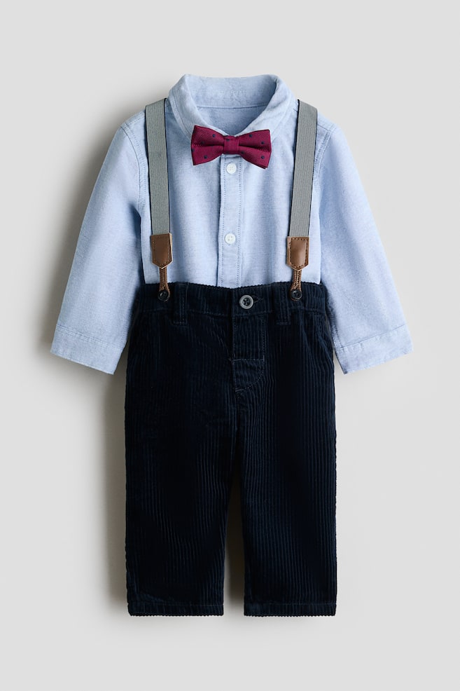 A childrenâs clothing set is shown from the front, featuring a light blue long-sleeve button-down shirt paired with navy blue corduroy trousers. The shirt features a textured burgundy bow tie at the collar, and striped grey suspenders with brown faux-leather tabs are attached to the trouser waistband. - 1