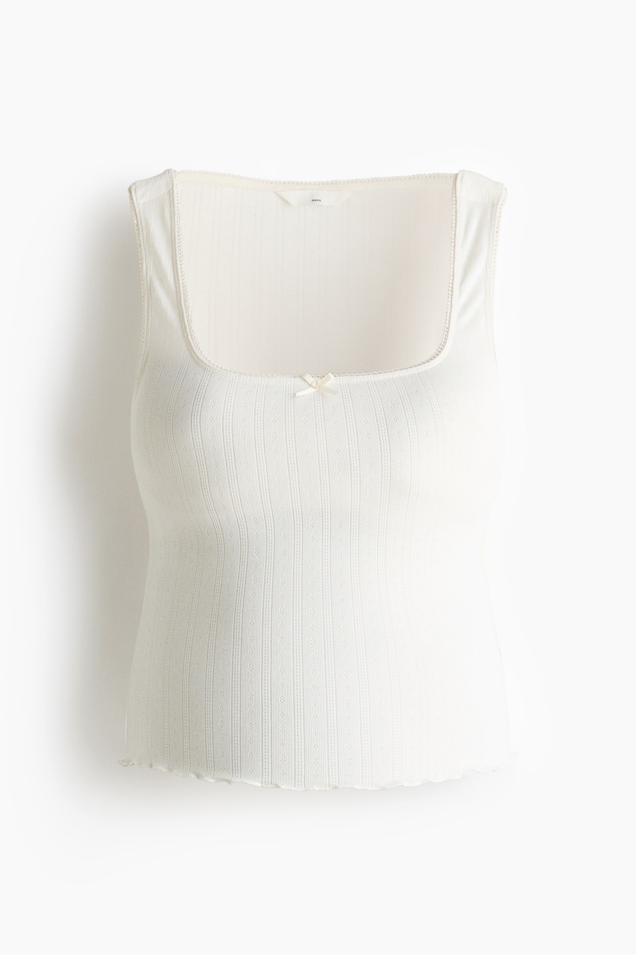 View larger image: A cream tank top featuring a square neckline with delicate lace trim and a small cream bow at the centre. It is crafted from a ribbed knit fabric with vertical eyelet details, and its hem is finished with a scalloped edge.